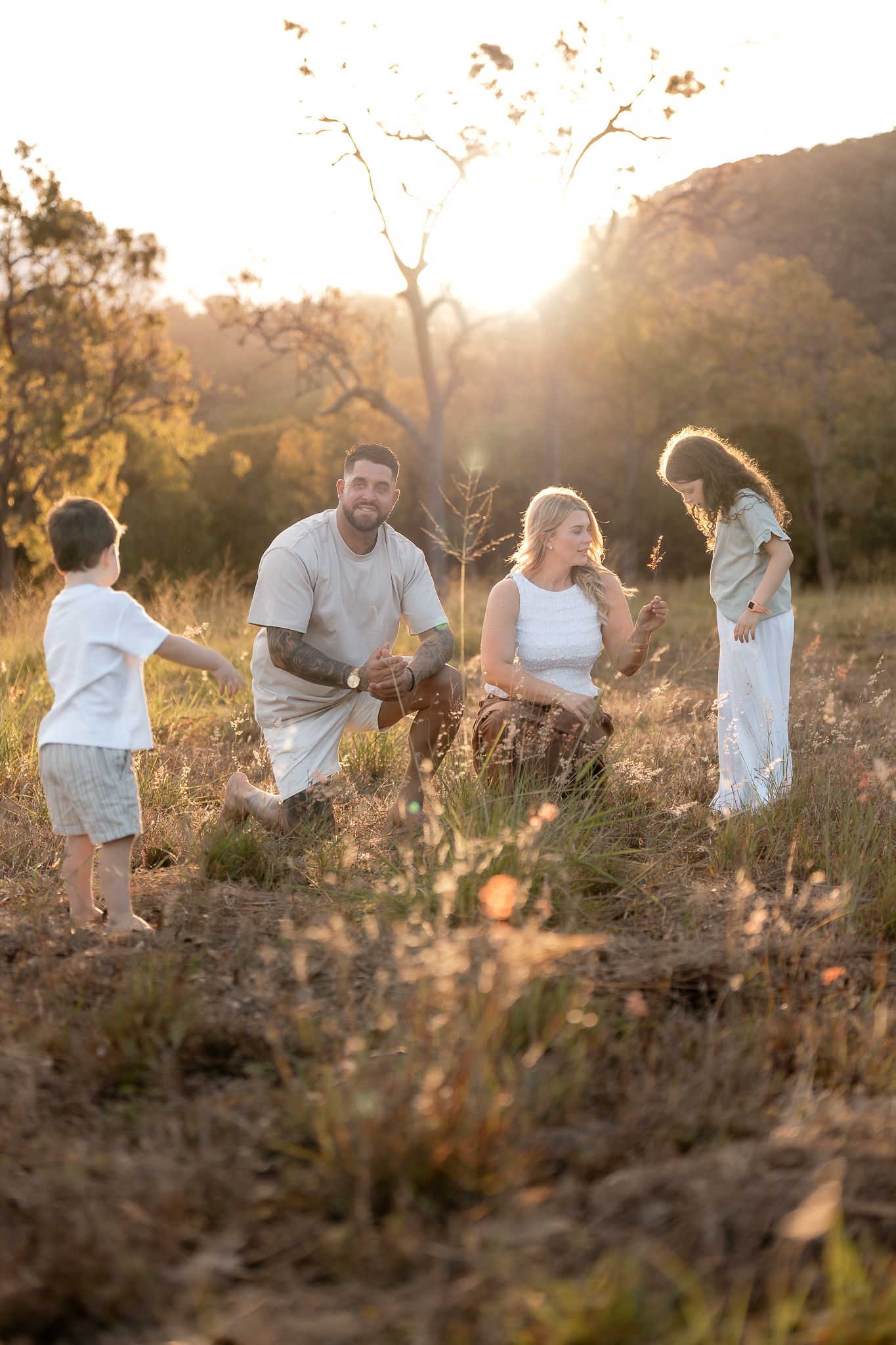 Joyful family of four playing together in golden sunlit field surrounded by trees at sunset.