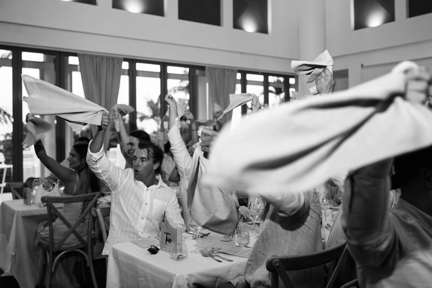 Guests wave white napkins in celebration at a wedding reception in a bright elegant venue.