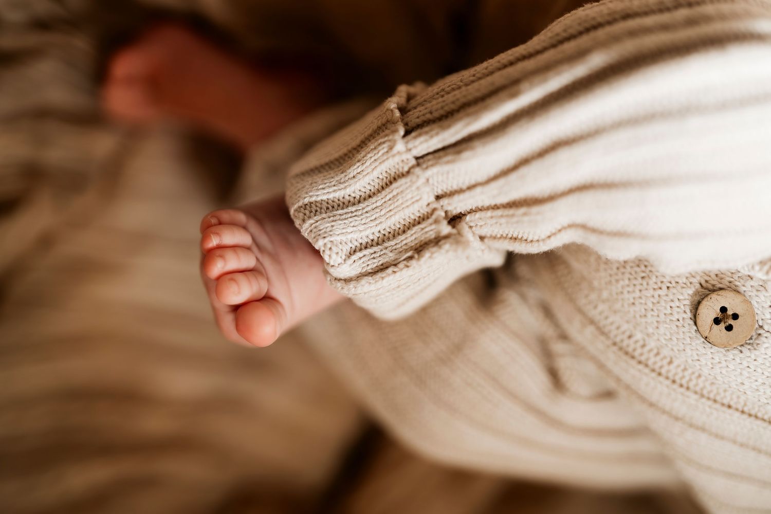 Close-up of newborn baby foot peeking out of cream knit outfit with button detail.