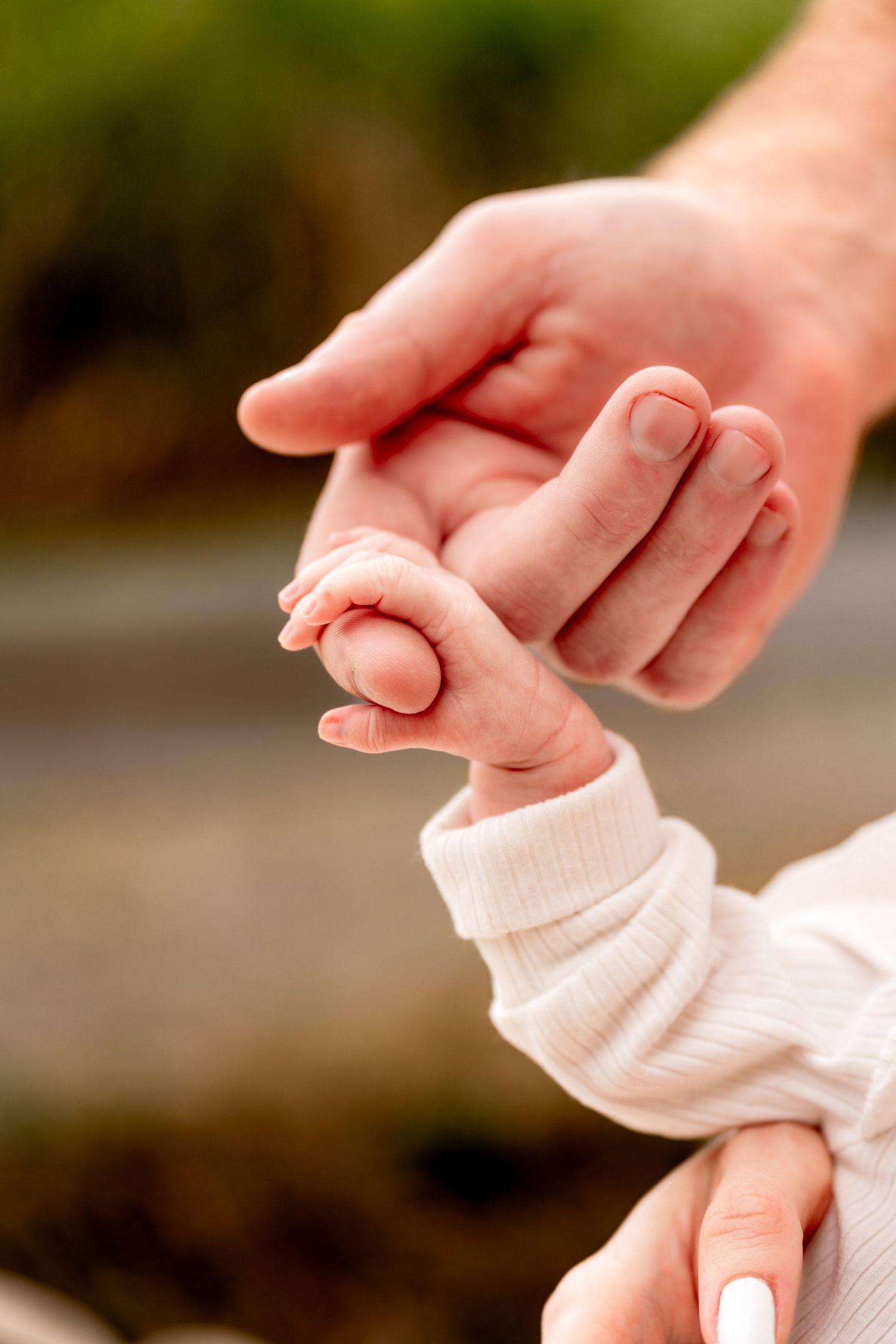 A newborn baby grasping an adult's finger in a tender close-up shot outdoors.