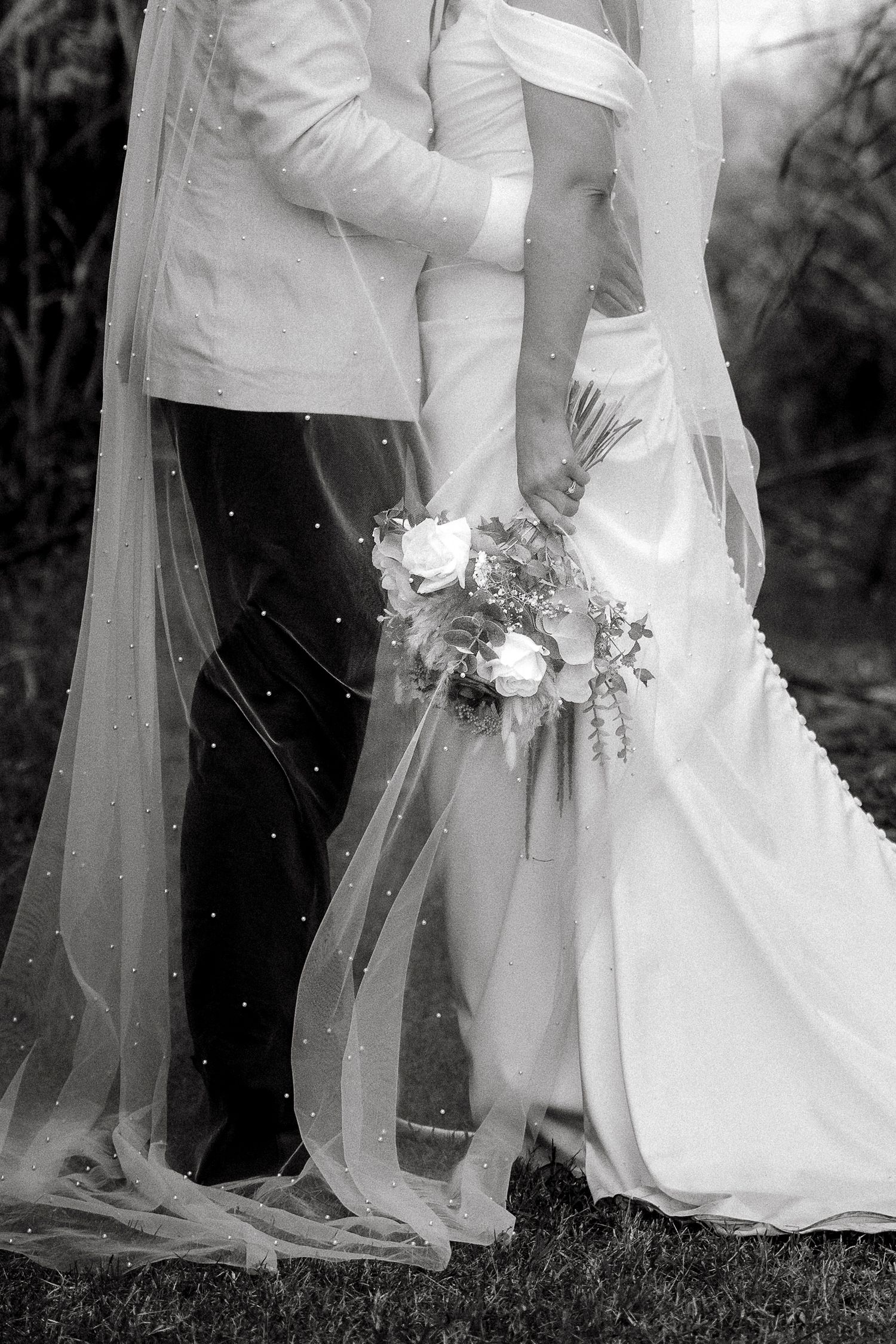 Black and white wedding photo of bride and groom holding hands, bride carrying bouquet with flowing veil.