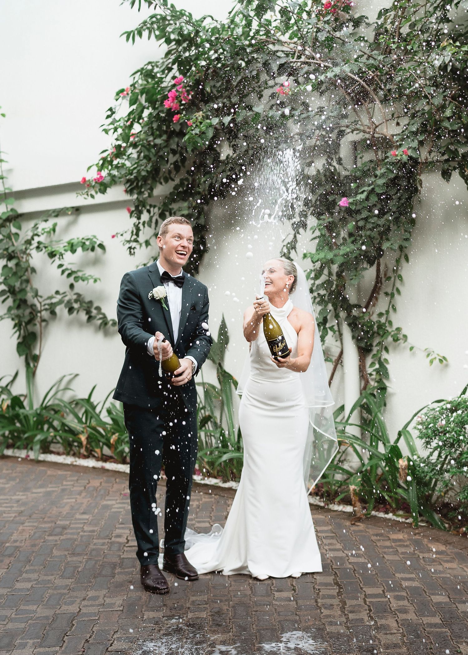 Bride and groom joyfully popping champagne bottles outdoors at their wedding celebration.