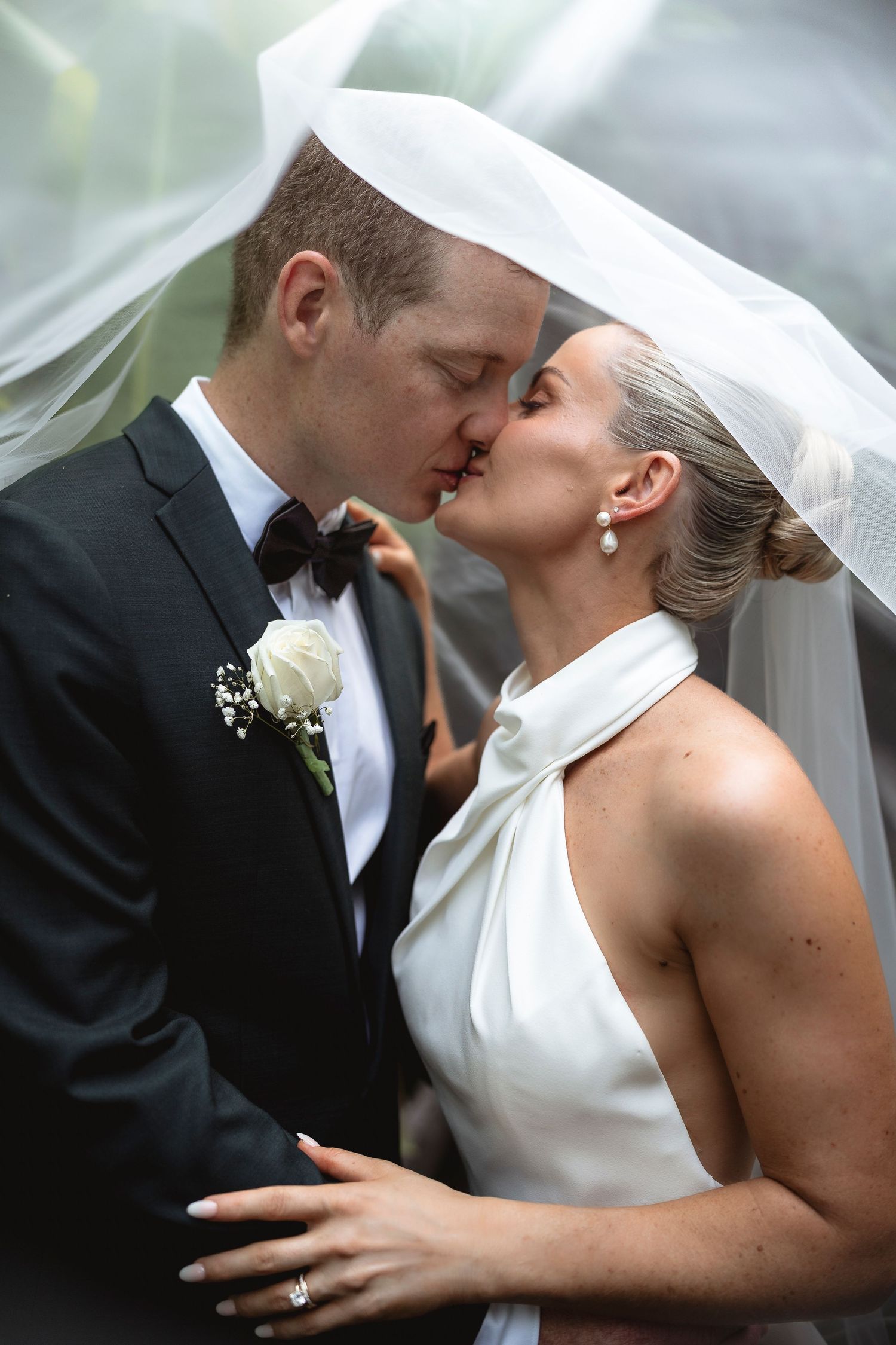 A bride and groom share a romantic kiss under a flowing white veil on their wedding day.