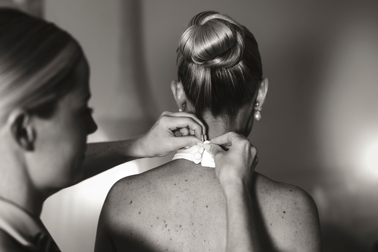 Black and white photo of a bridesmaid tying a bow on the back of a bride's elegant wedding dress.