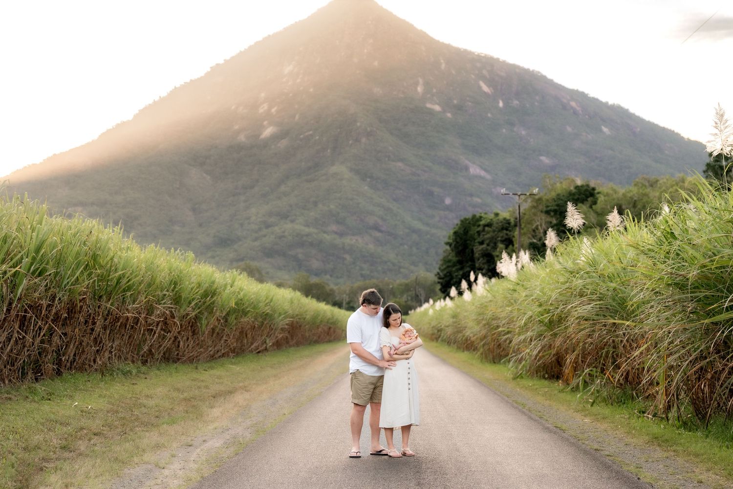 Couple embracing on a quiet rural road surrounded by sugarcane fields with volcanic mountain backdrop.