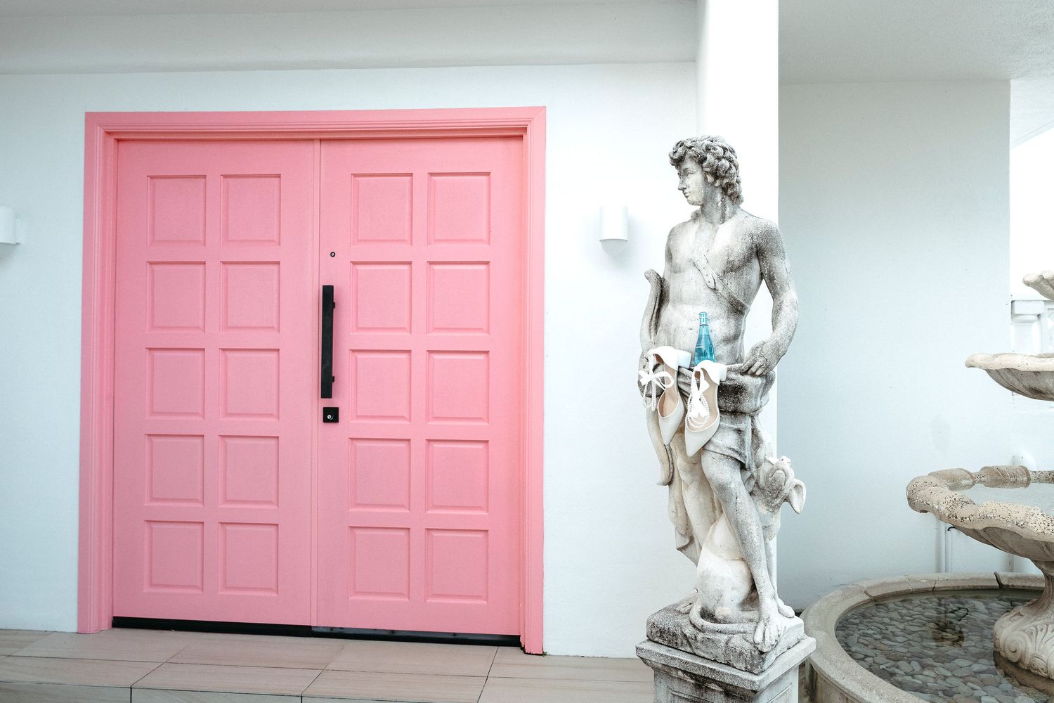 Classical marble statue beside a vibrant pink double door entrance with fountain.