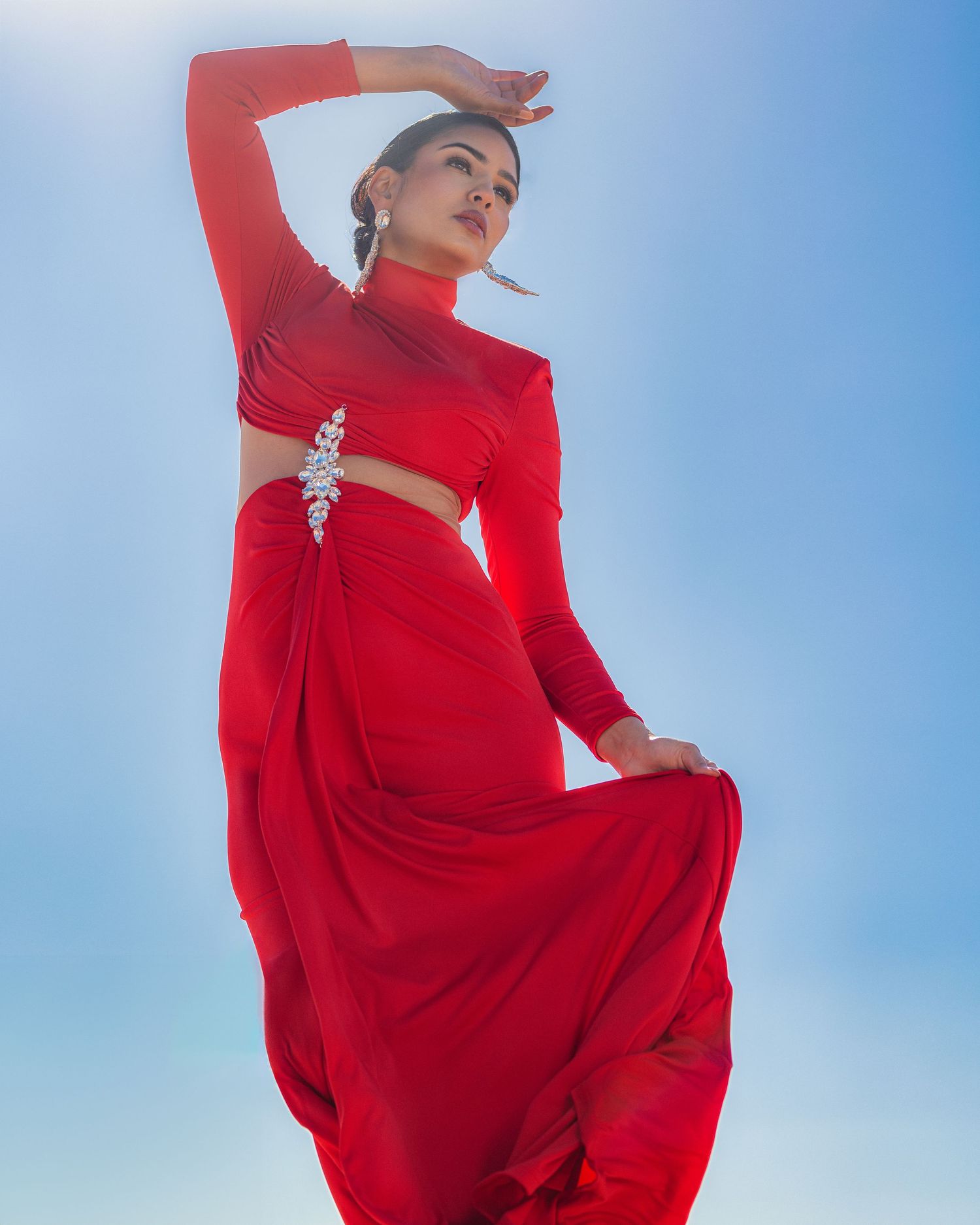 A graceful figure in a flowing red dress twirls against a bright blue sky background, creating a striking contrast.