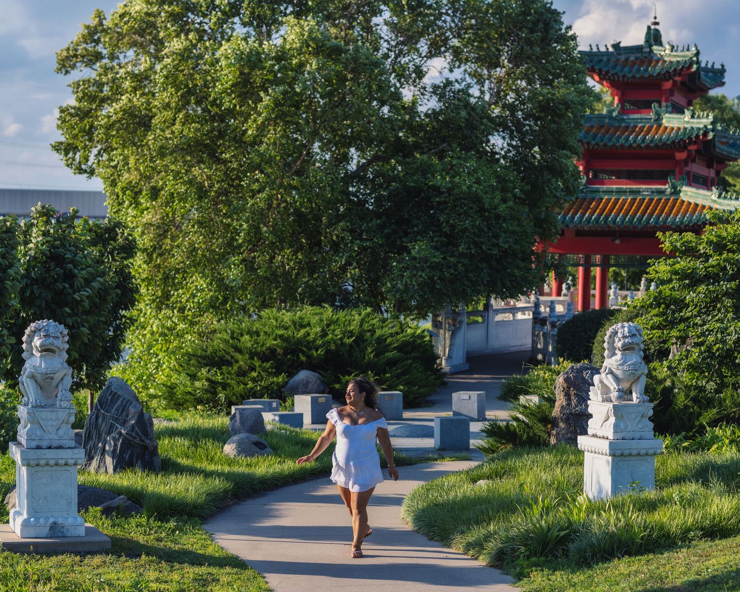 A peaceful path leads through a Chinese garden with lion statues and a traditional pagoda tower in the background.