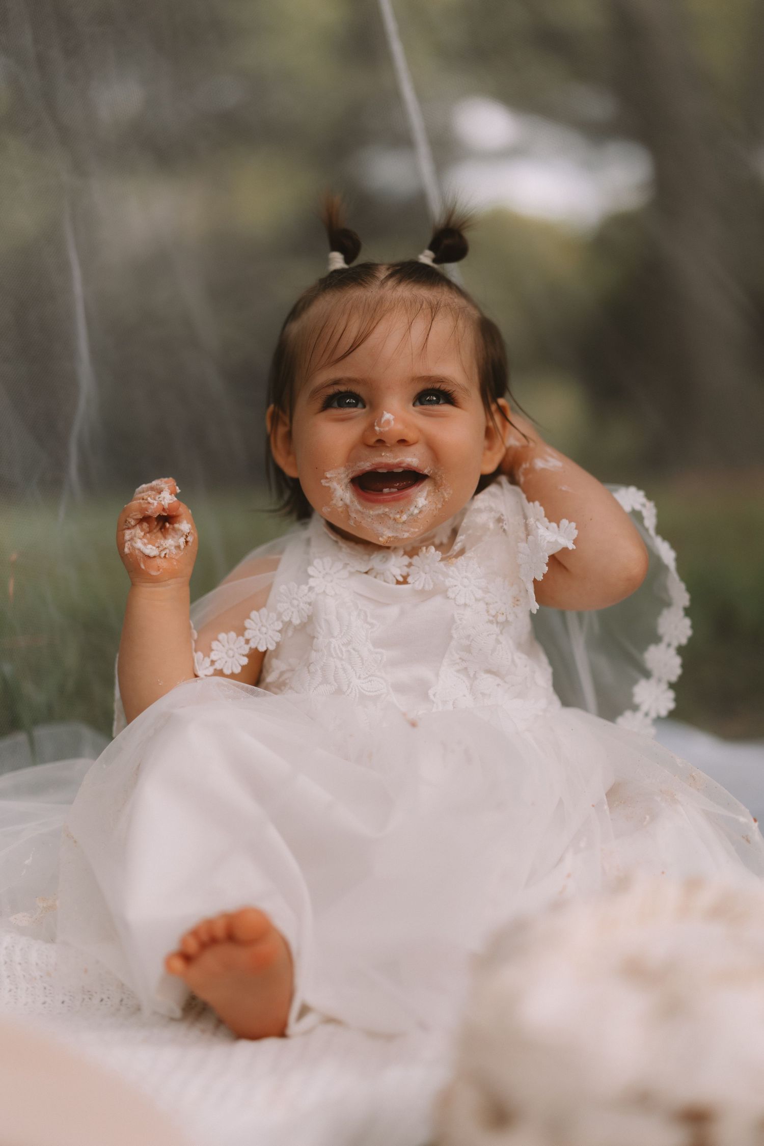 A joyful baby in a white dress plays with delicate white feathers during a whimsical photo session.