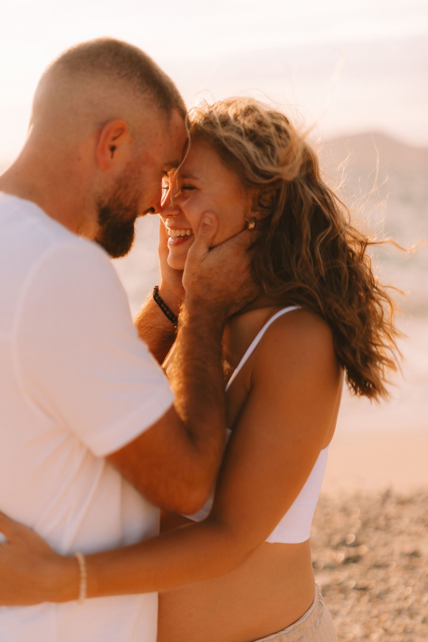 A romantic couple shares intimate moments at sunset on a sandy beach in warm golden light.