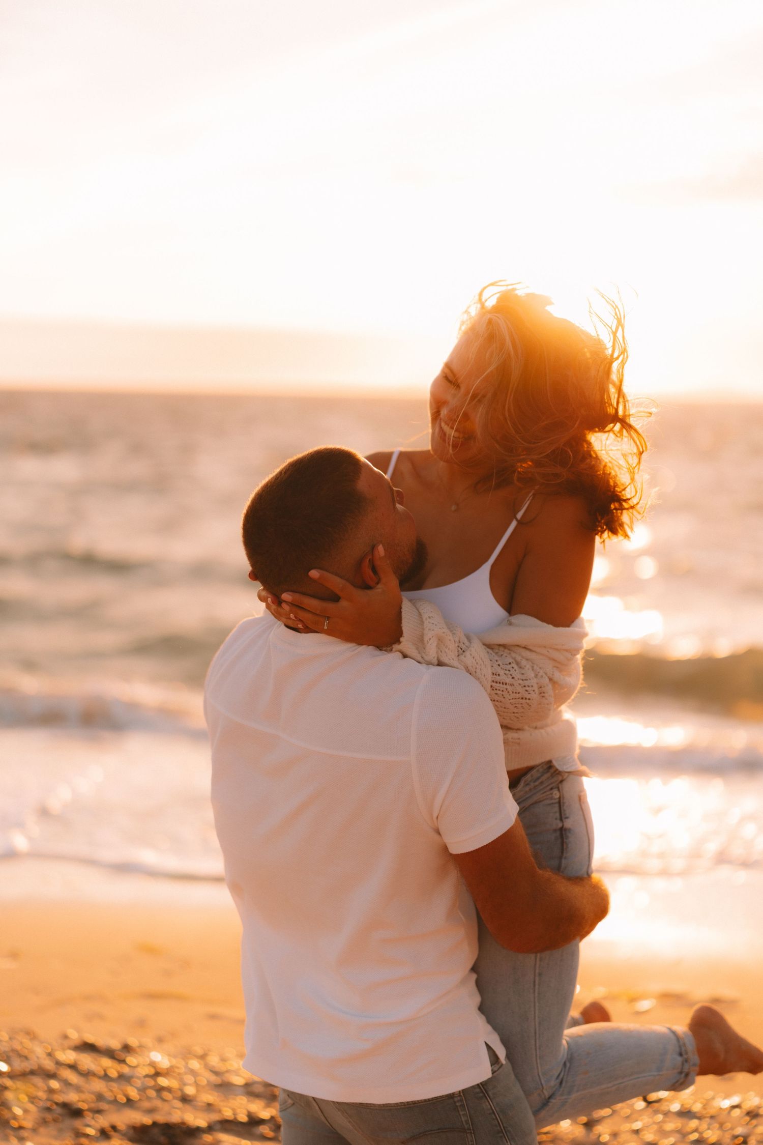 Couple embraces on a sandy beach at sunset creating a romantic silhouette against the golden sky.