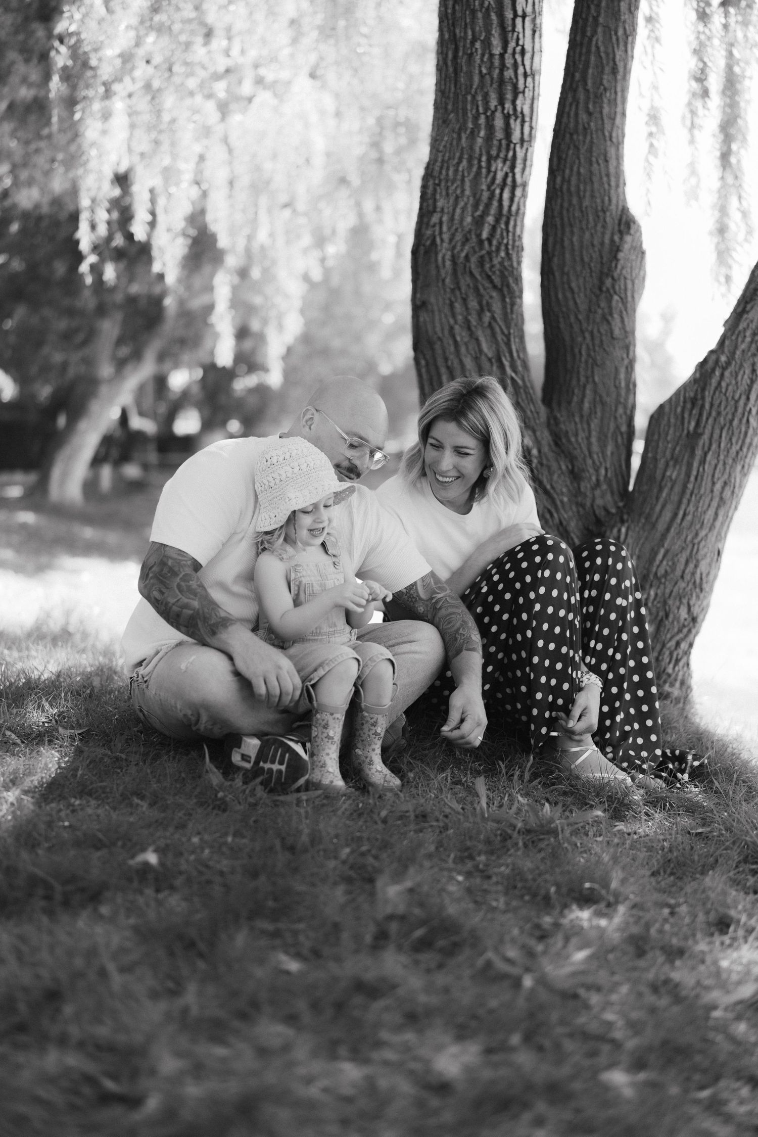 A family shares a tender moment together while sitting under a large tree on a sunny afternoon.