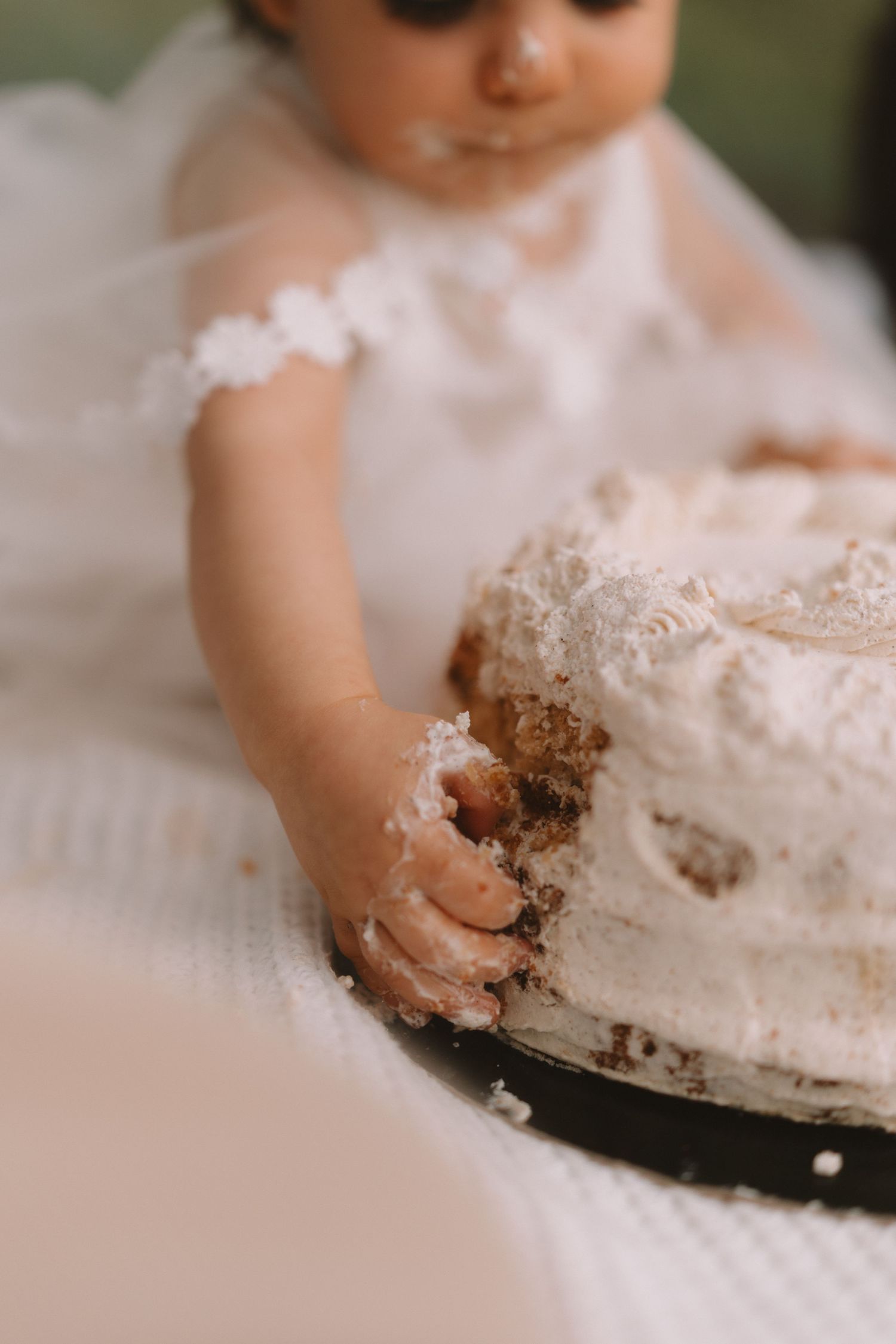 Small hands reach out to grab and smear white frosting on what appears to be a cake or dessert surface.