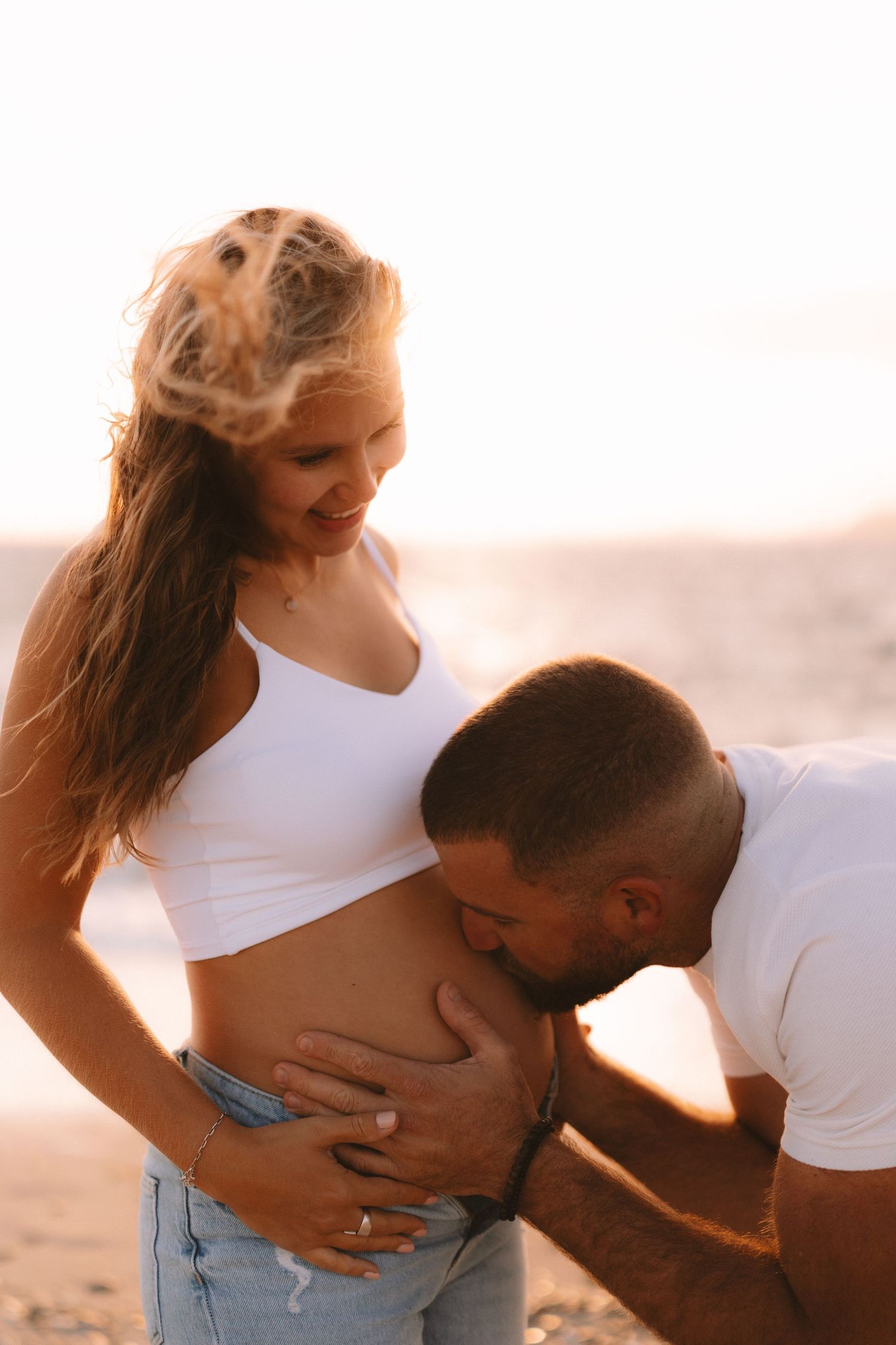A couple shares an intimate moment on the beach at sunset, silhouetted against the warm golden light.