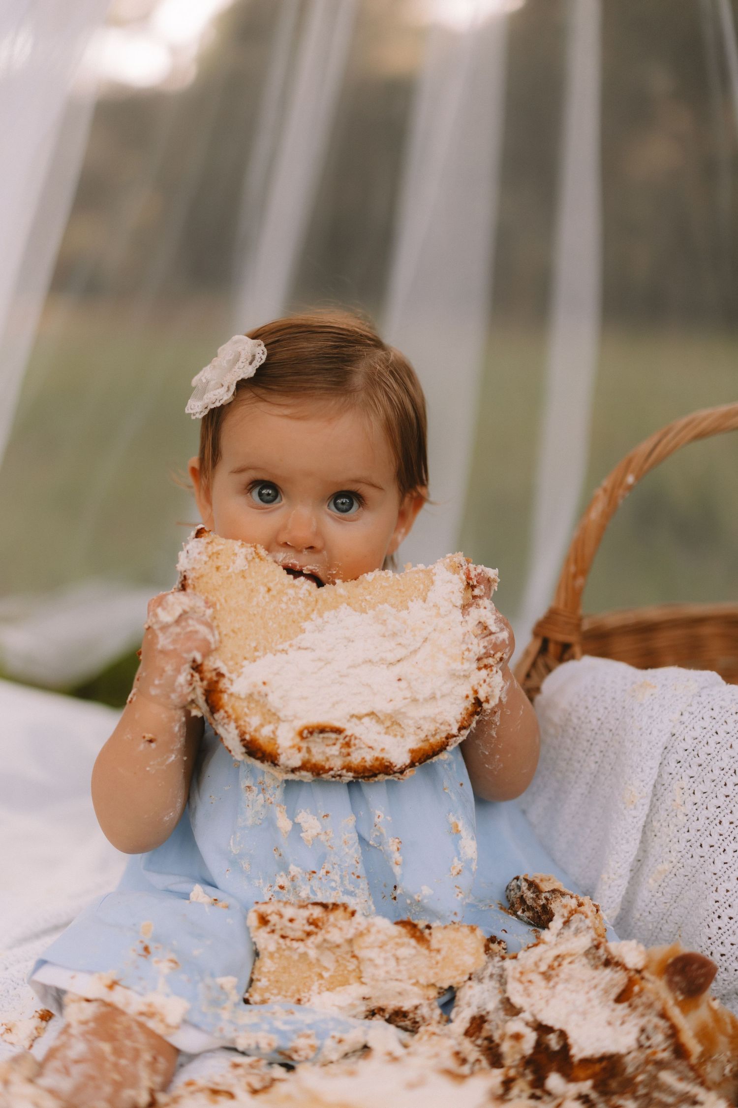 A baby wearing a blue dress gets covered in cake and frosting during a festive cake smash photoshoot.