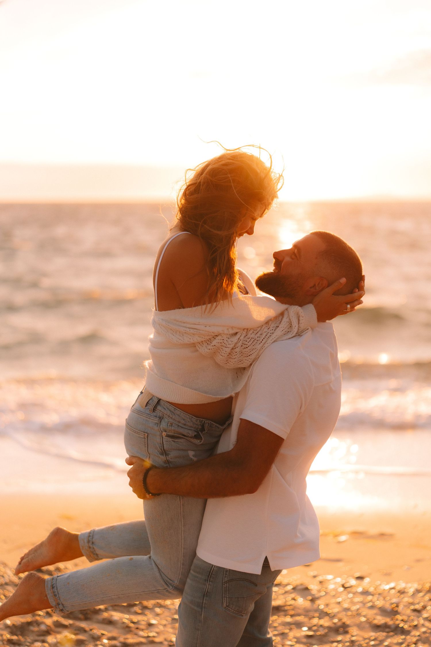 Romantic couple embracing on a beach at sunset with golden light illuminating their silhouettes.