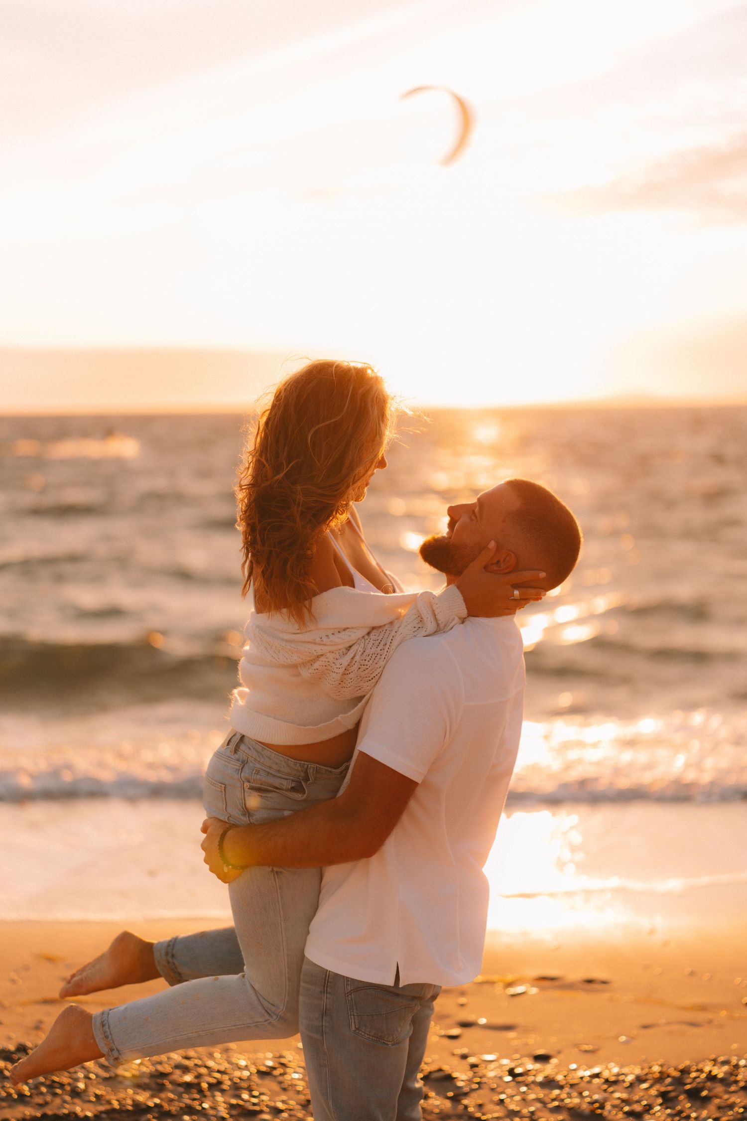 Tender moment between two people on the beach during a warm sunset with waves in the background.