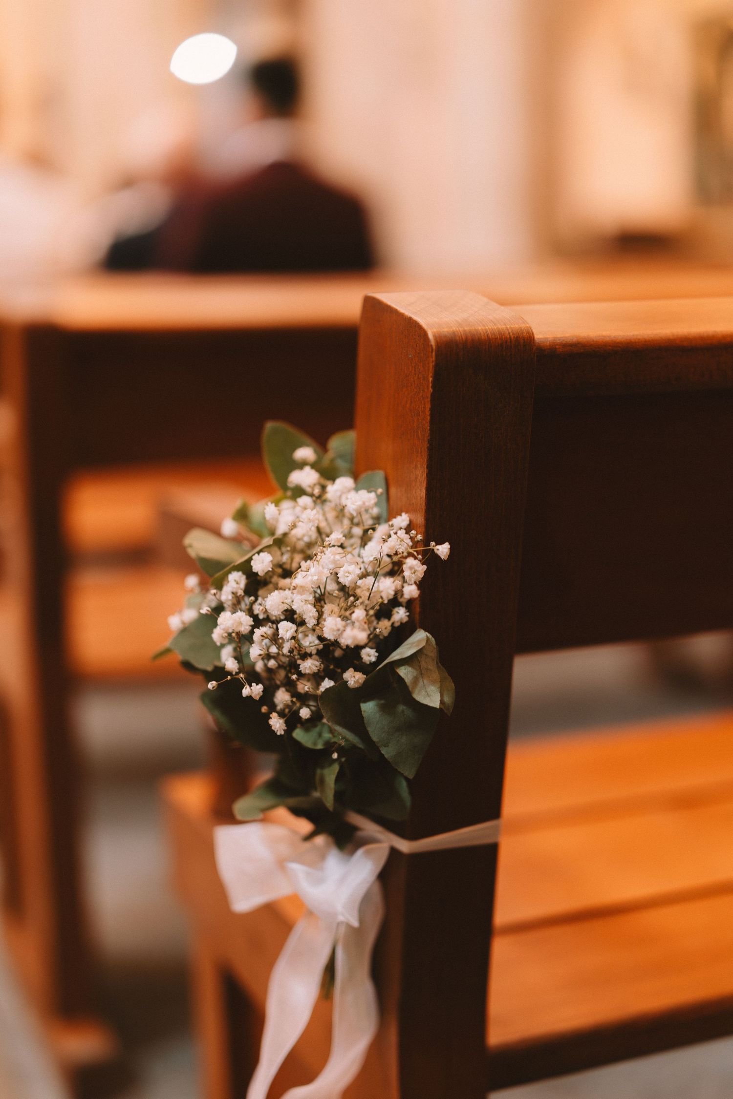 Church pews decorated with delicate baby's breath and white ribbon bouquets for a wedding ceremony.