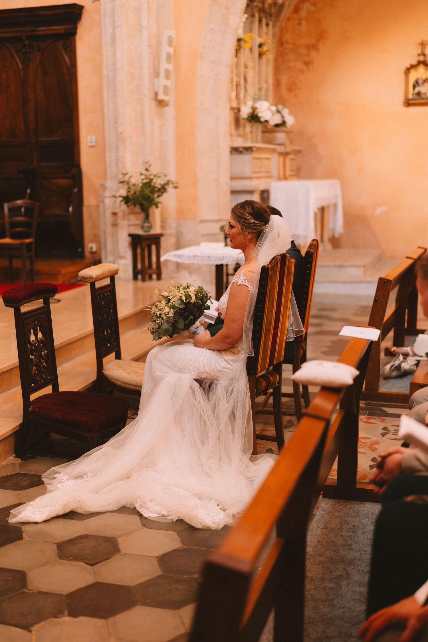A flowing white wedding dress drapes elegantly across wooden church pews in a warmly lit sanctuary.