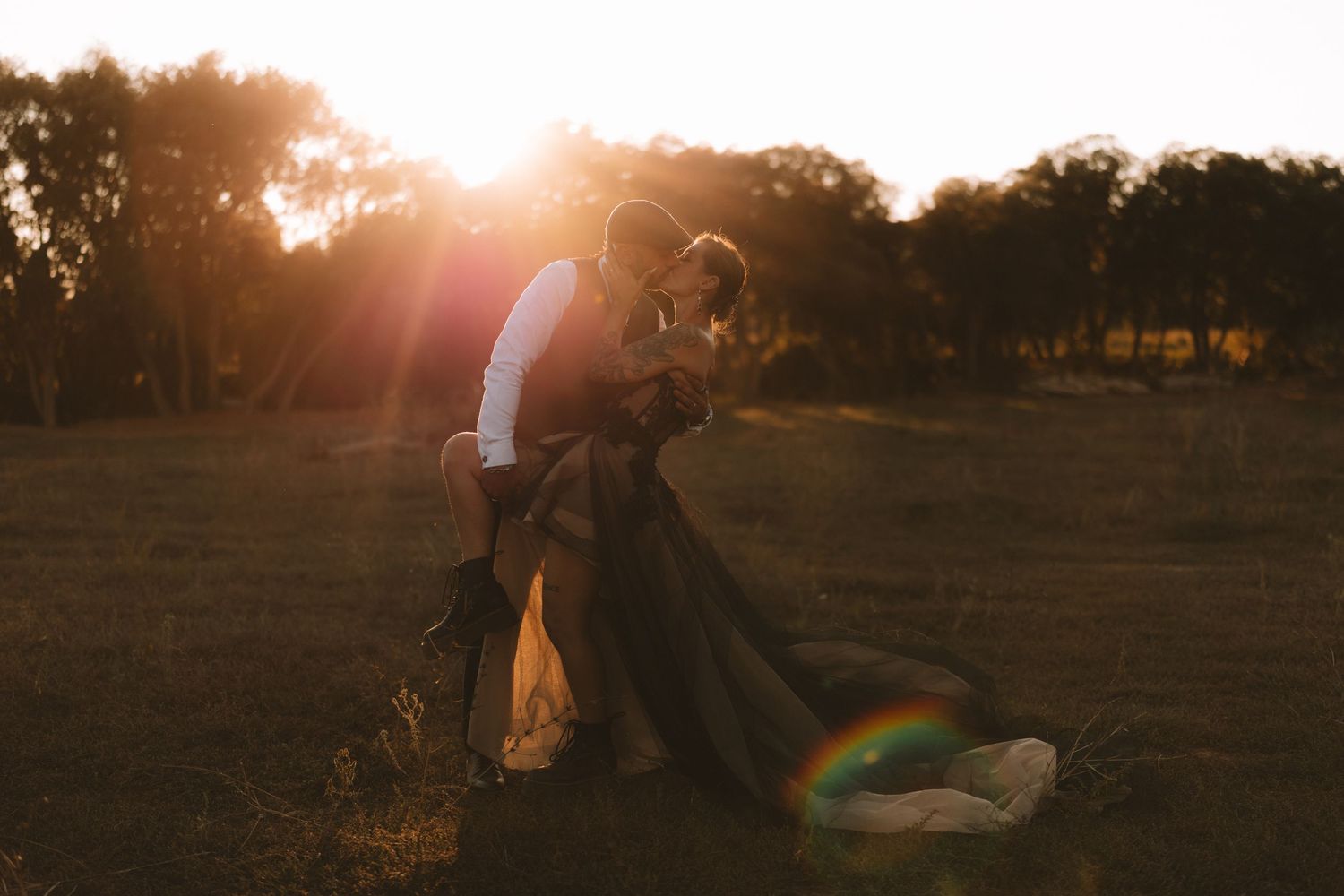 Silhouetted figures walk across a grassy field at sunset with golden sunlight streaming through the trees.