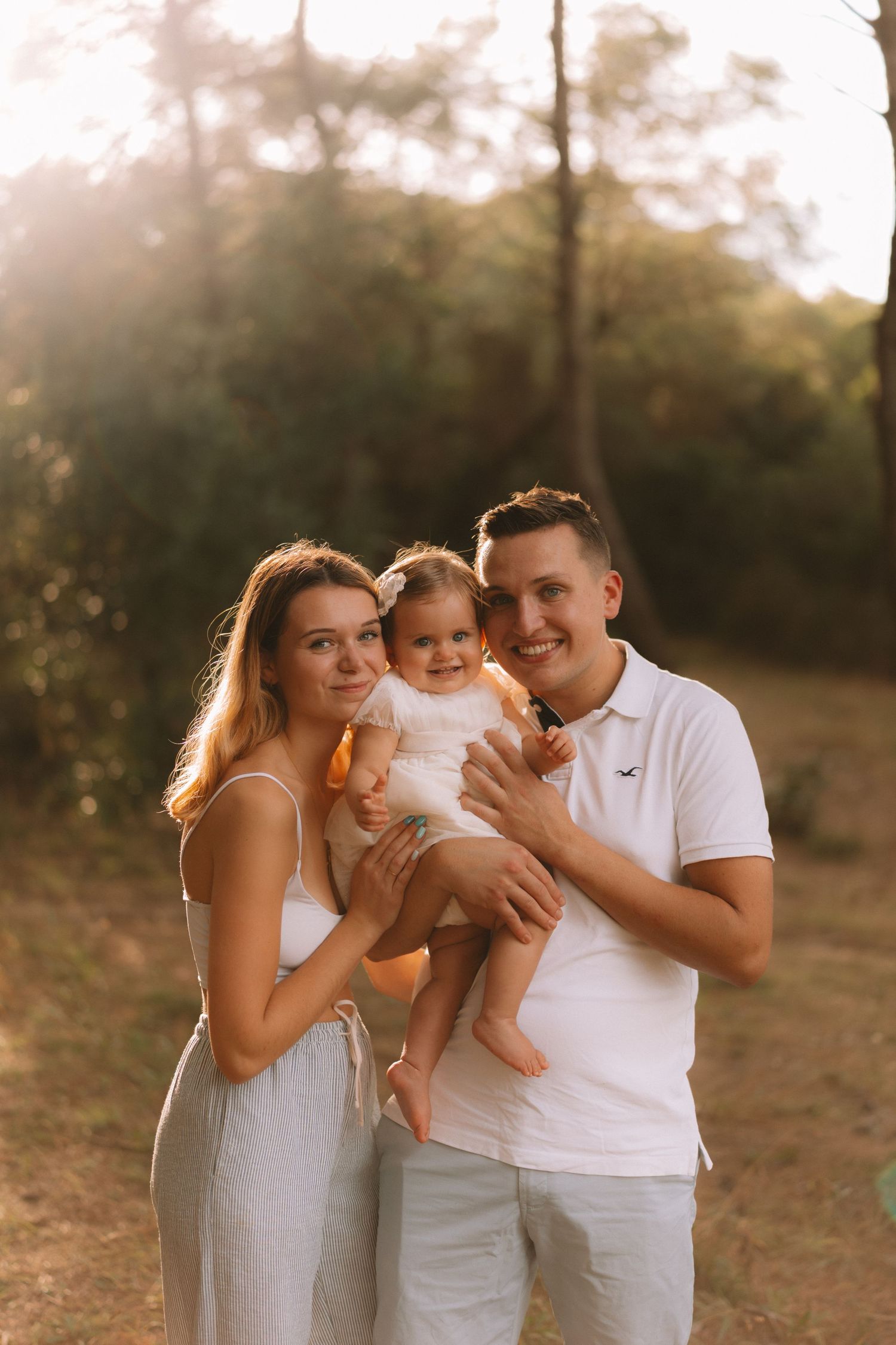 A family wearing white outfits embraces during a golden sunset photo session outdoors.