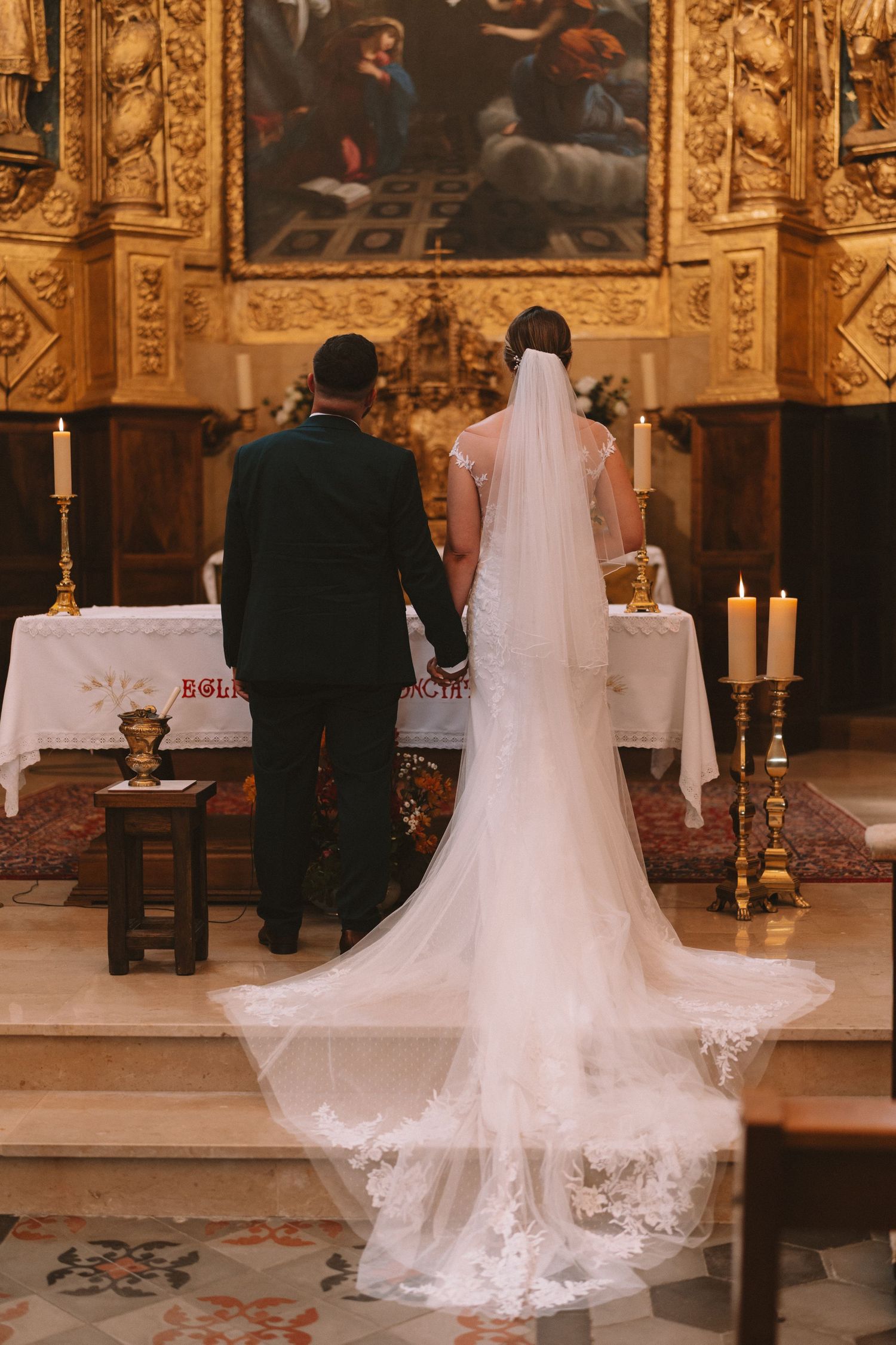 A bride's veil and wedding dress train cascade beautifully across the floor of an ornate church during a ceremony.