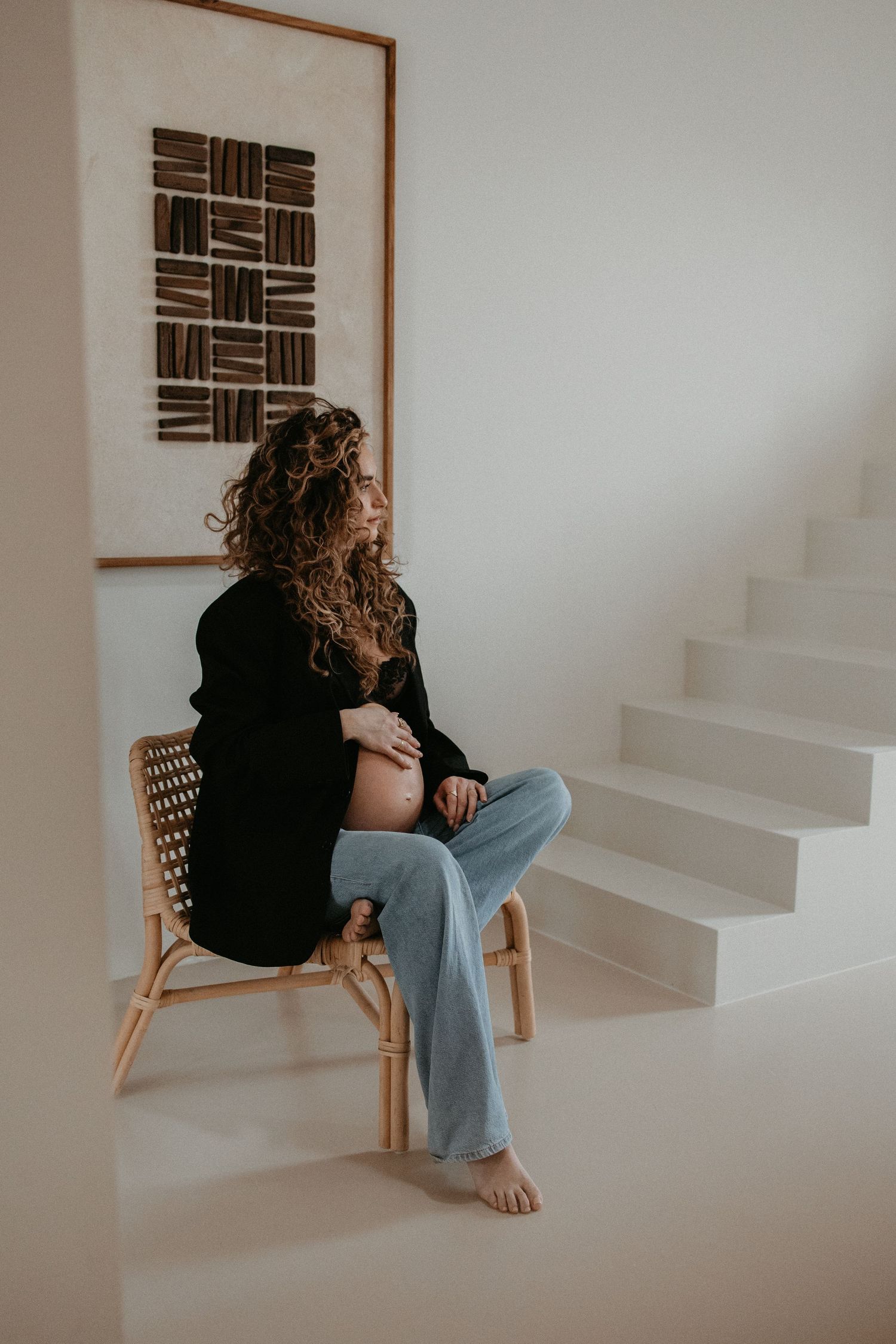 Intiem portret van een zwangere vrouw zittend, haar hand liefdevol op haar buik, in een lichte en rustige huiselijke sfeer