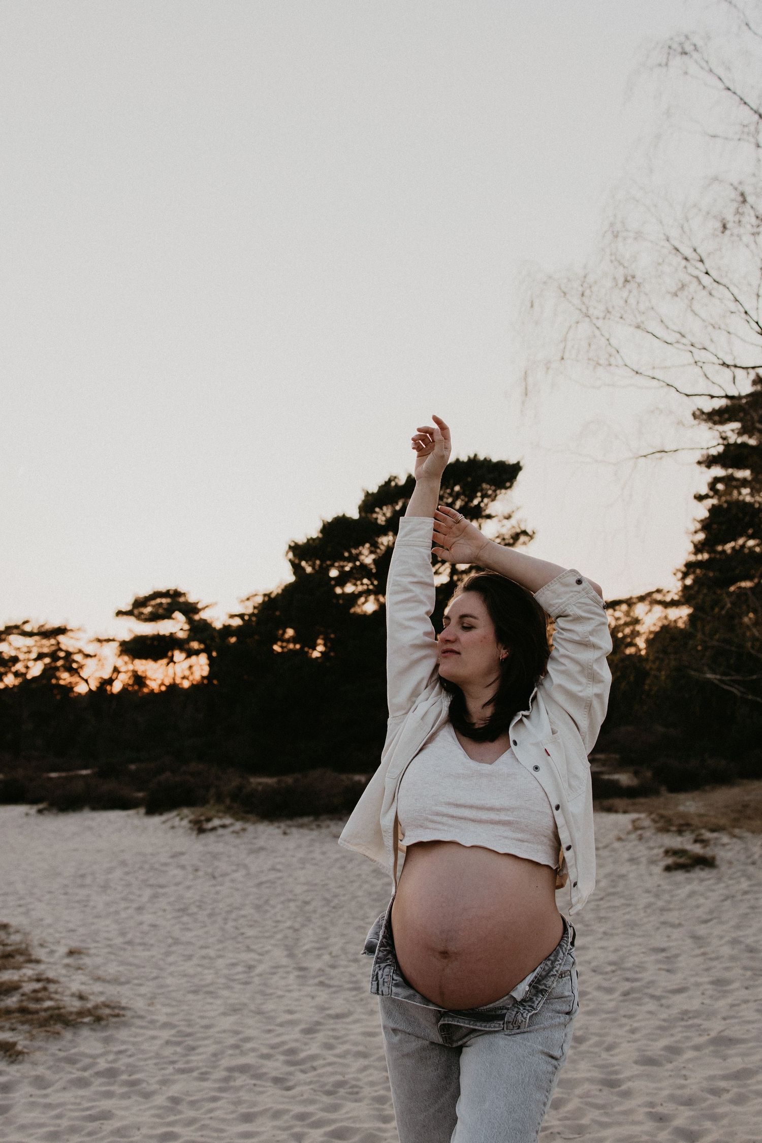 Zwangere vrouw in jeans en een open blouse laat haar buik zien terwijl ze geniet