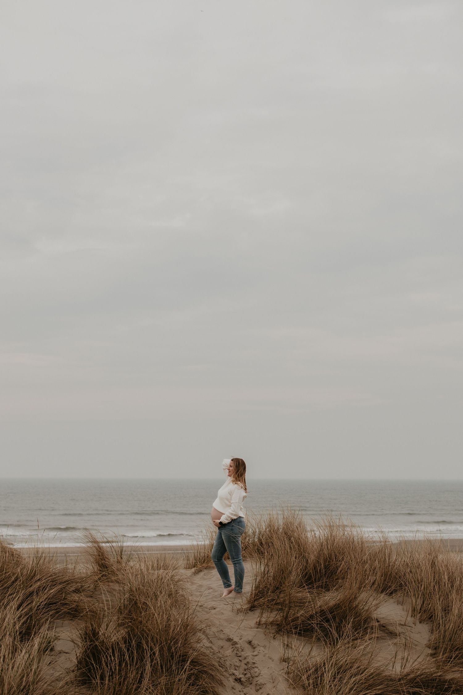 In de duinen bij de zee staat een krachtige zwangere vrouw