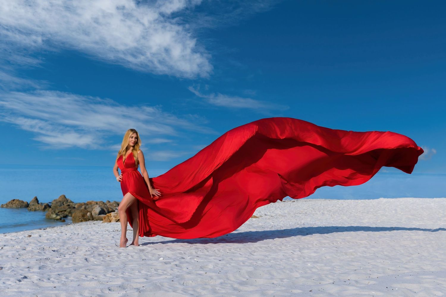 A flowing red dress fabric creates a dramatic contrast against pristine white snow and bright blue sky. Flying Dress photoshoot Naples Fl