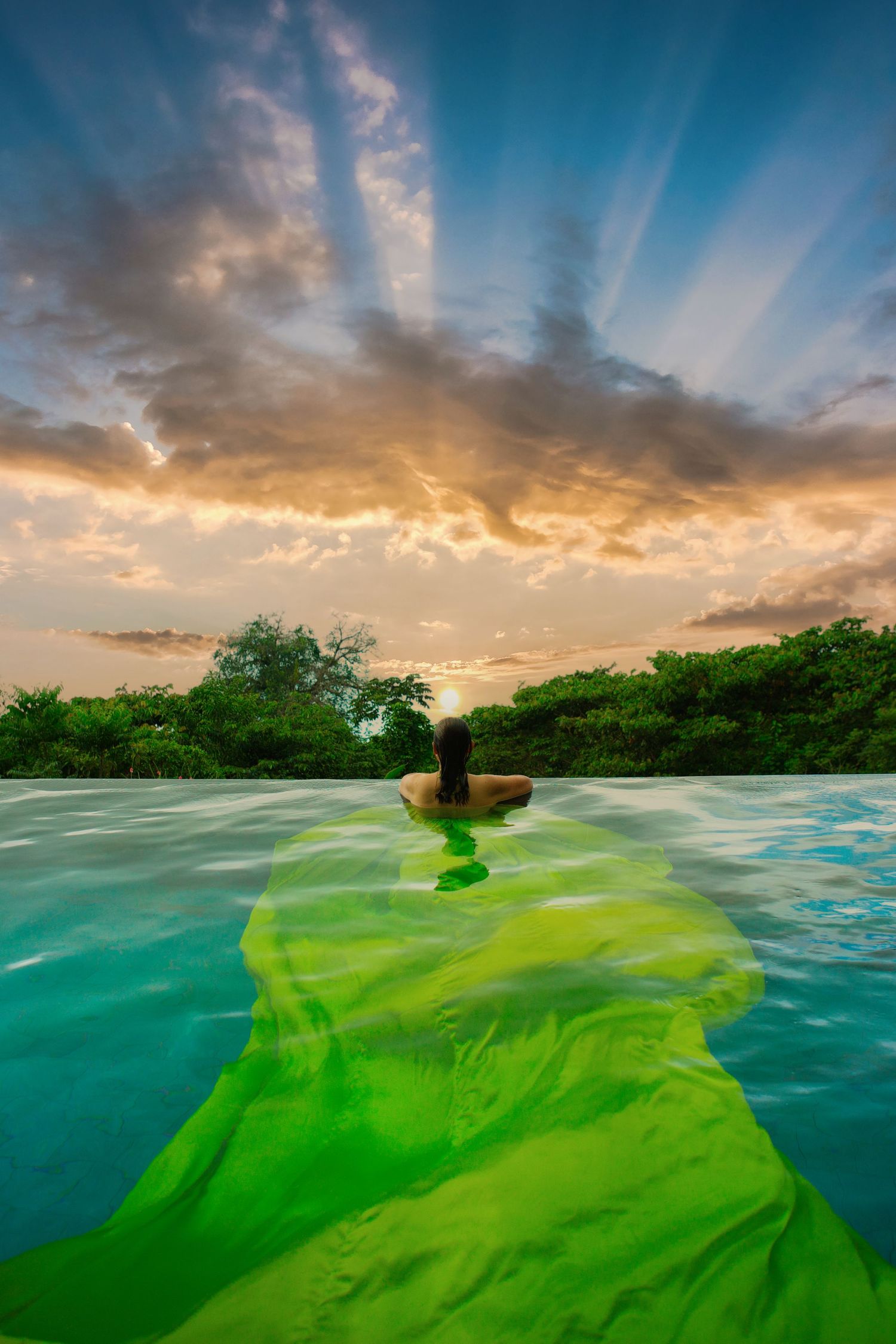 Dramatic sunset over ocean with split-view underwater showing bright green seaweed moving with the current. Flying Dress Photoshoot
