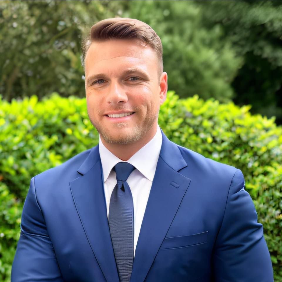 Business portrait of person wearing blue suit against green landscaping.