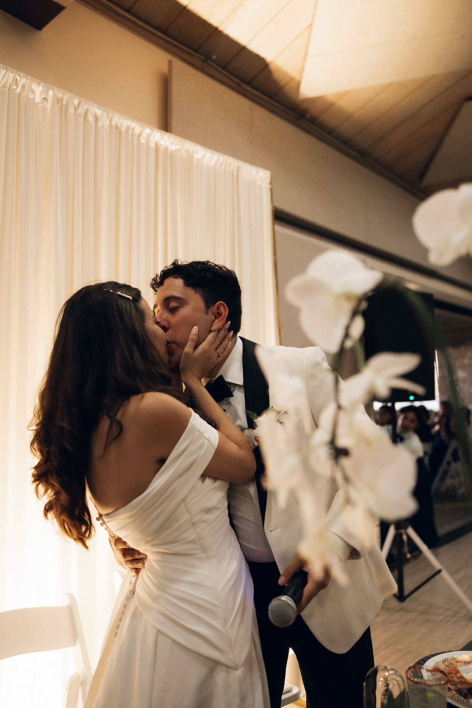 A couple shares a romantic kiss during their wedding celebration with white curtains in the background.