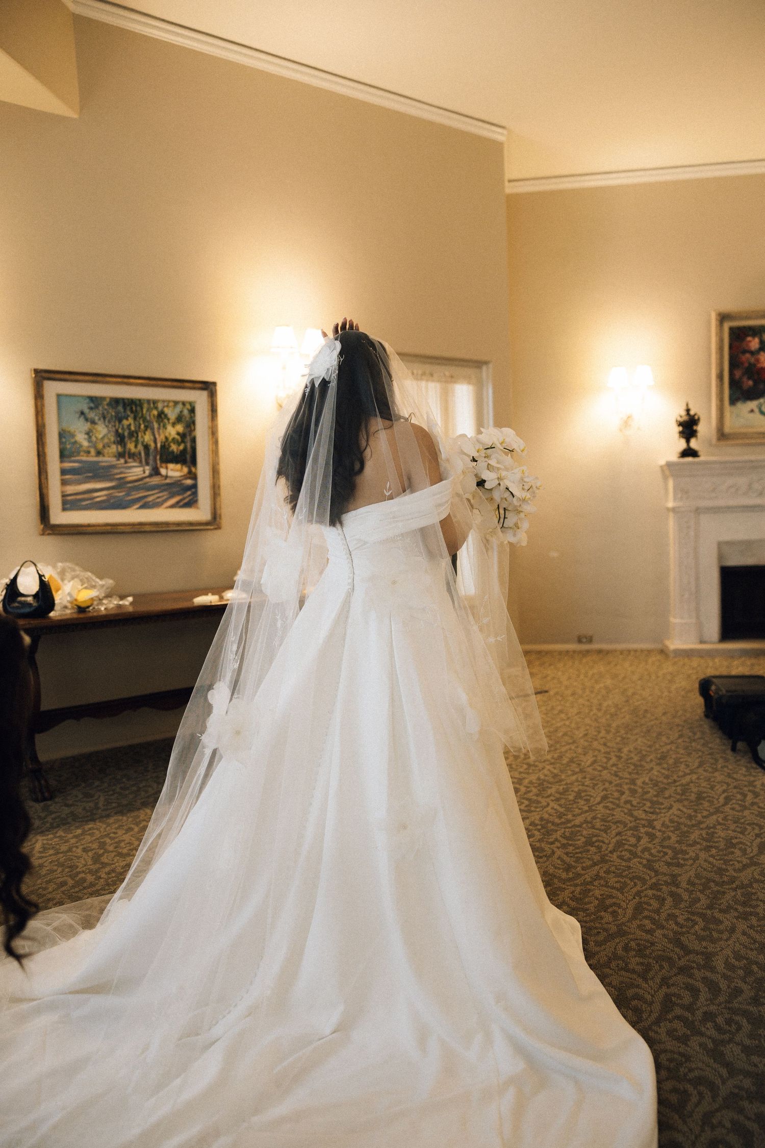 A flowing white wedding dress with cathedral length veil displayed in an elegant hotel room with warm lighting.
