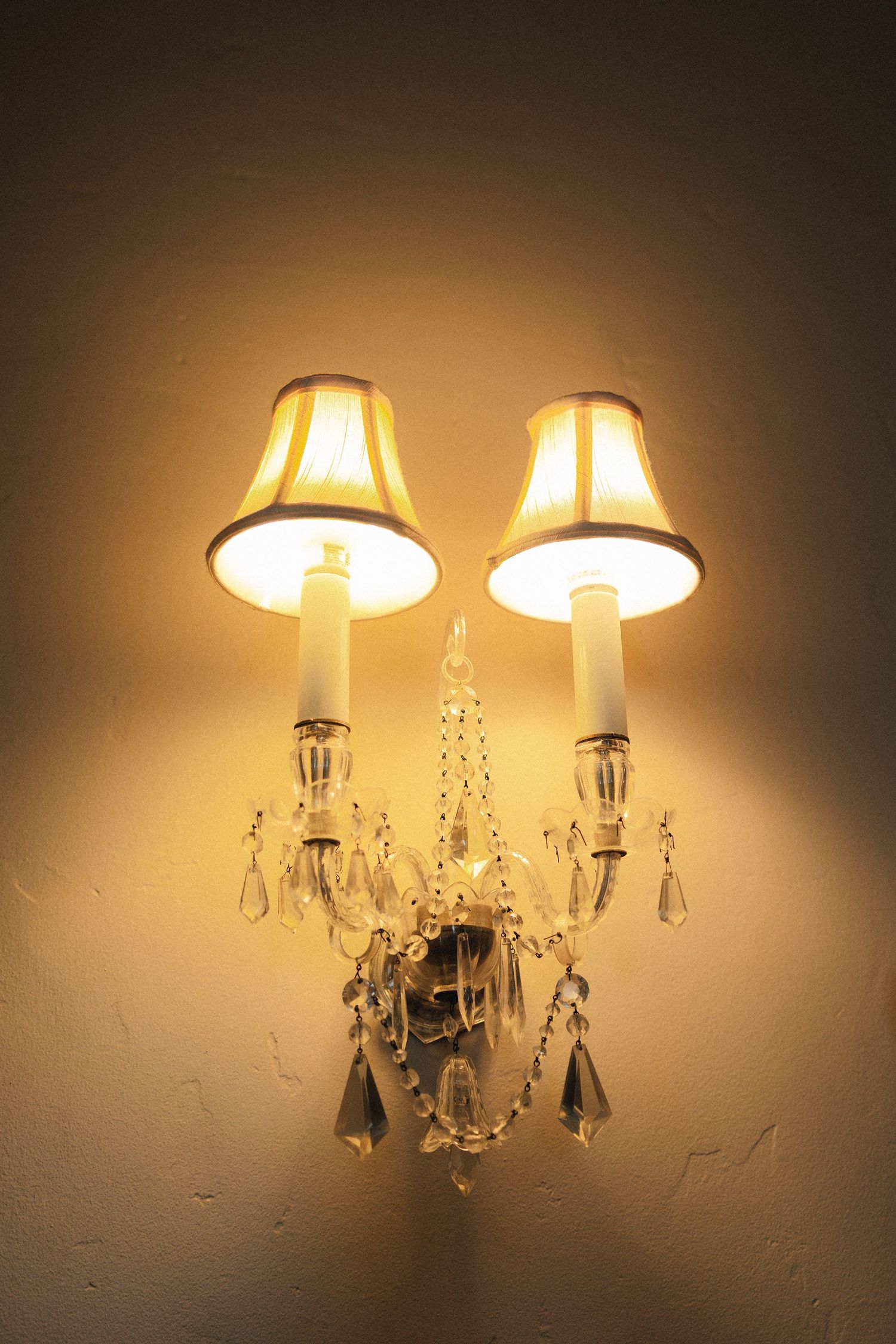 Crystal wall sconce with illuminated lampshades casting warm ambient light in a dark room.
