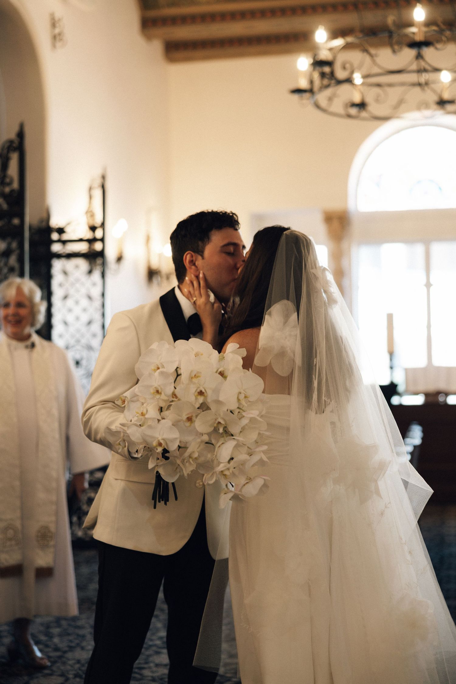 Elegant wedding ceremony moment with white orchid bouquet and flowing veil in a beautifully lit venue.