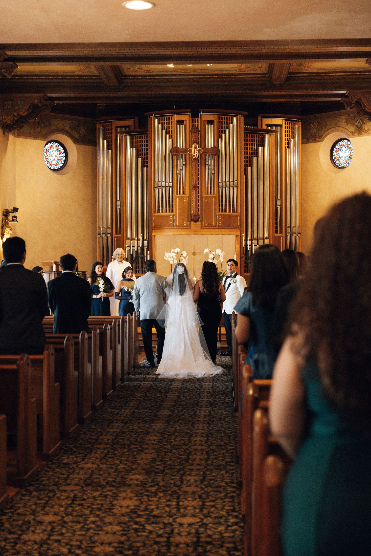 Wedding ceremony in a traditional church with wooden pews and a large pipe organ at the altar.