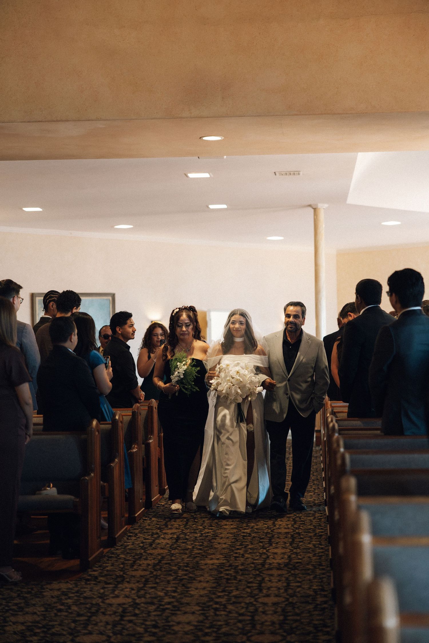A line of people stand in church pews during what appears to be a wedding ceremony or religious service.
