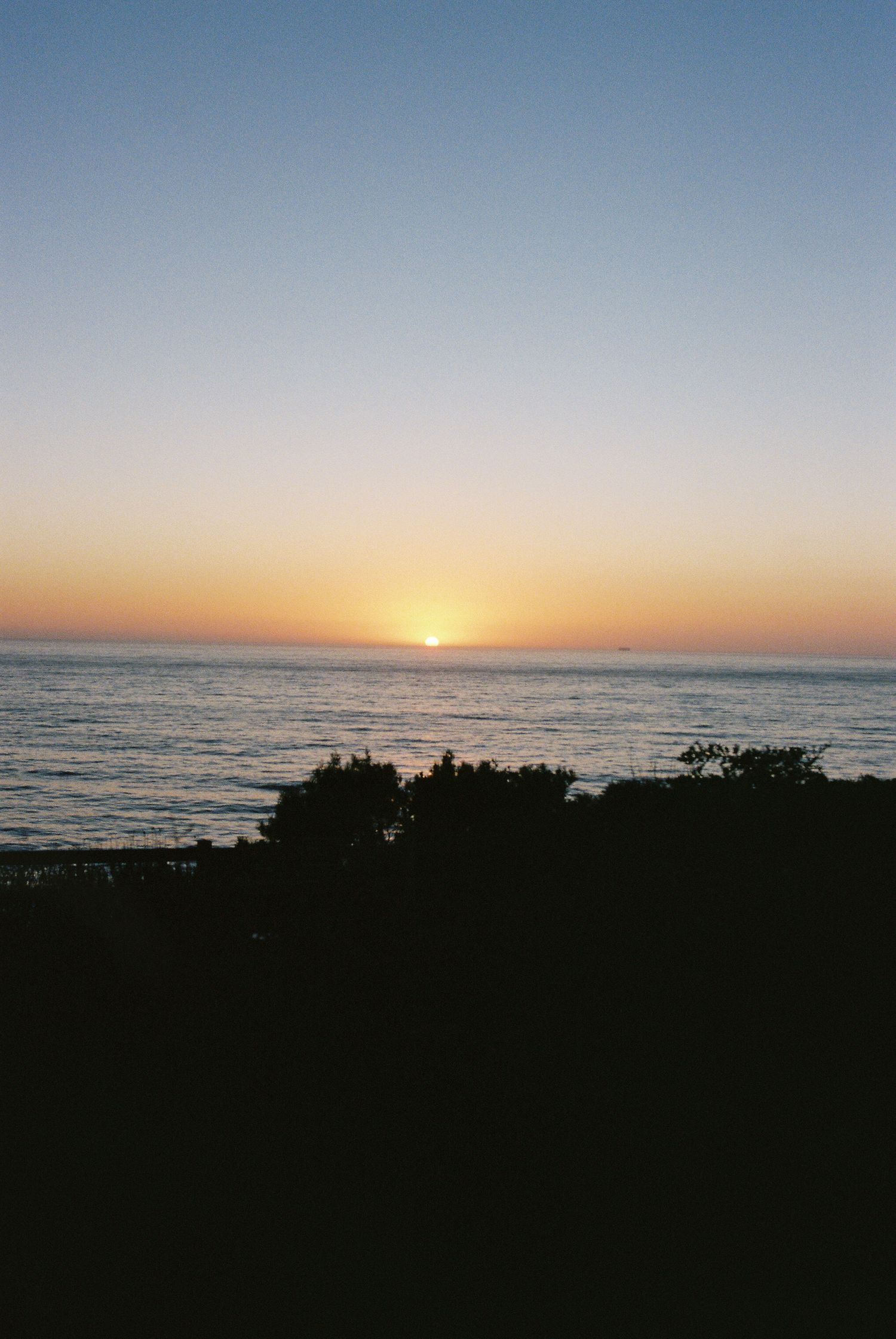 A series of sunset photos over the ocean horizon showing the progression from dusk to dark with silhouetted coastline.