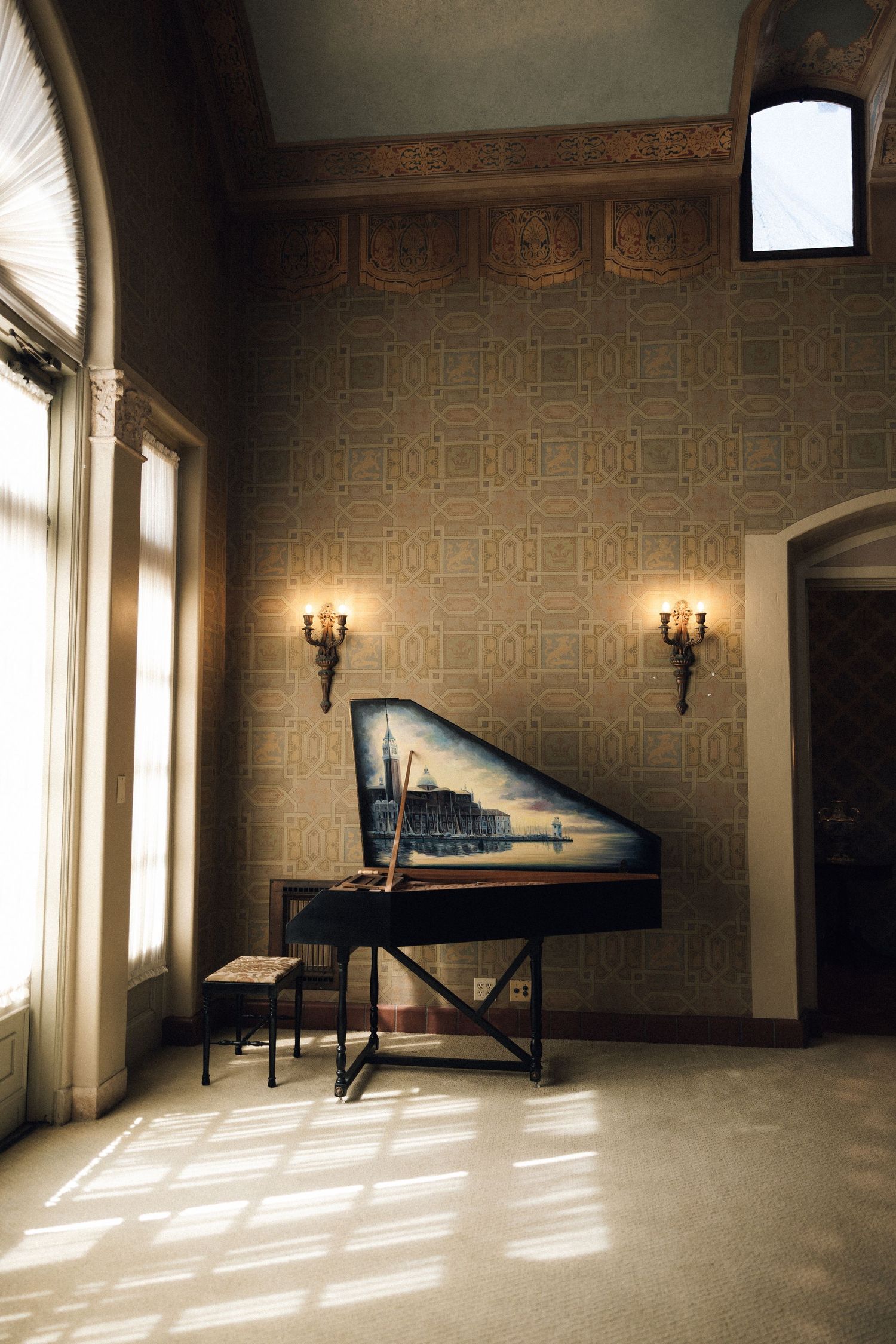 Sunlight streams through windows into an empty vintage room with ornate wallpaper and a solitary massage table.