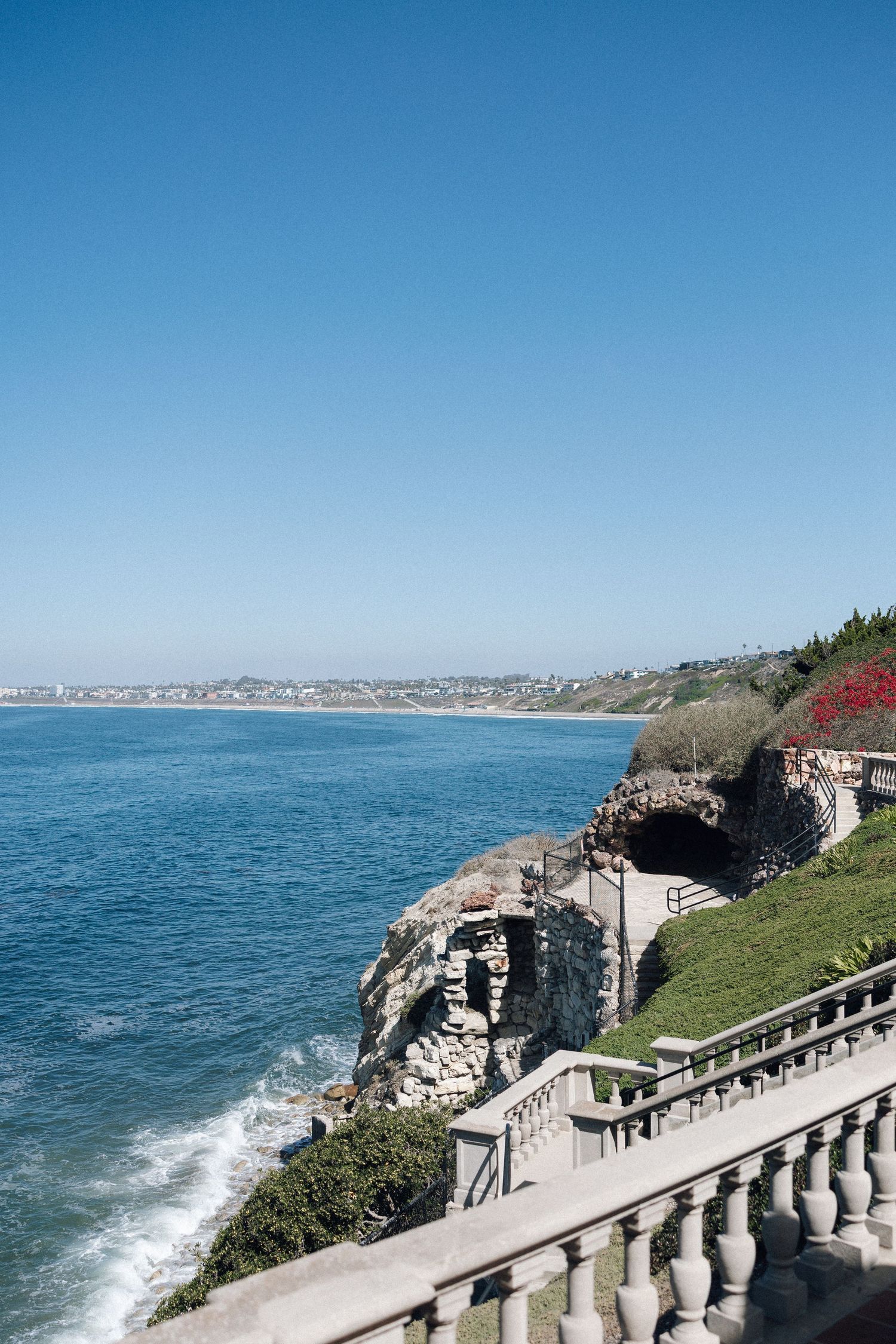 Scenic coastal cliffs with a stone balustrade walkway overlooking the Pacific Ocean on a clear blue day.