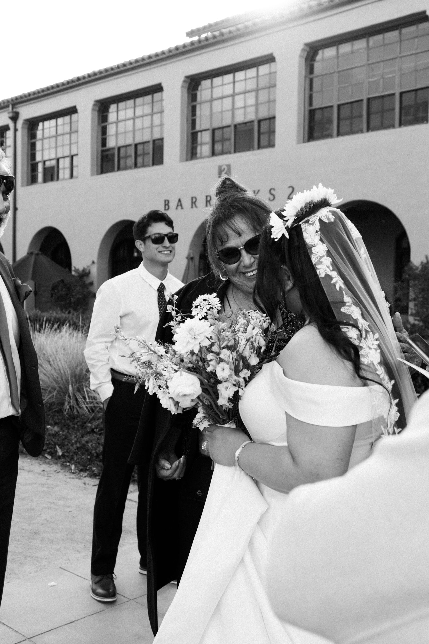 A black and white wedding photo showing people celebrating outside a Spanish-style building with arched windows.