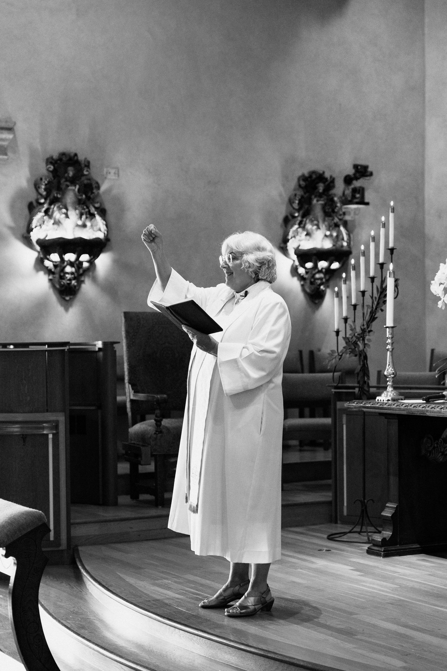 A person in white robes reads from a book during a religious service in a church sanctuary.