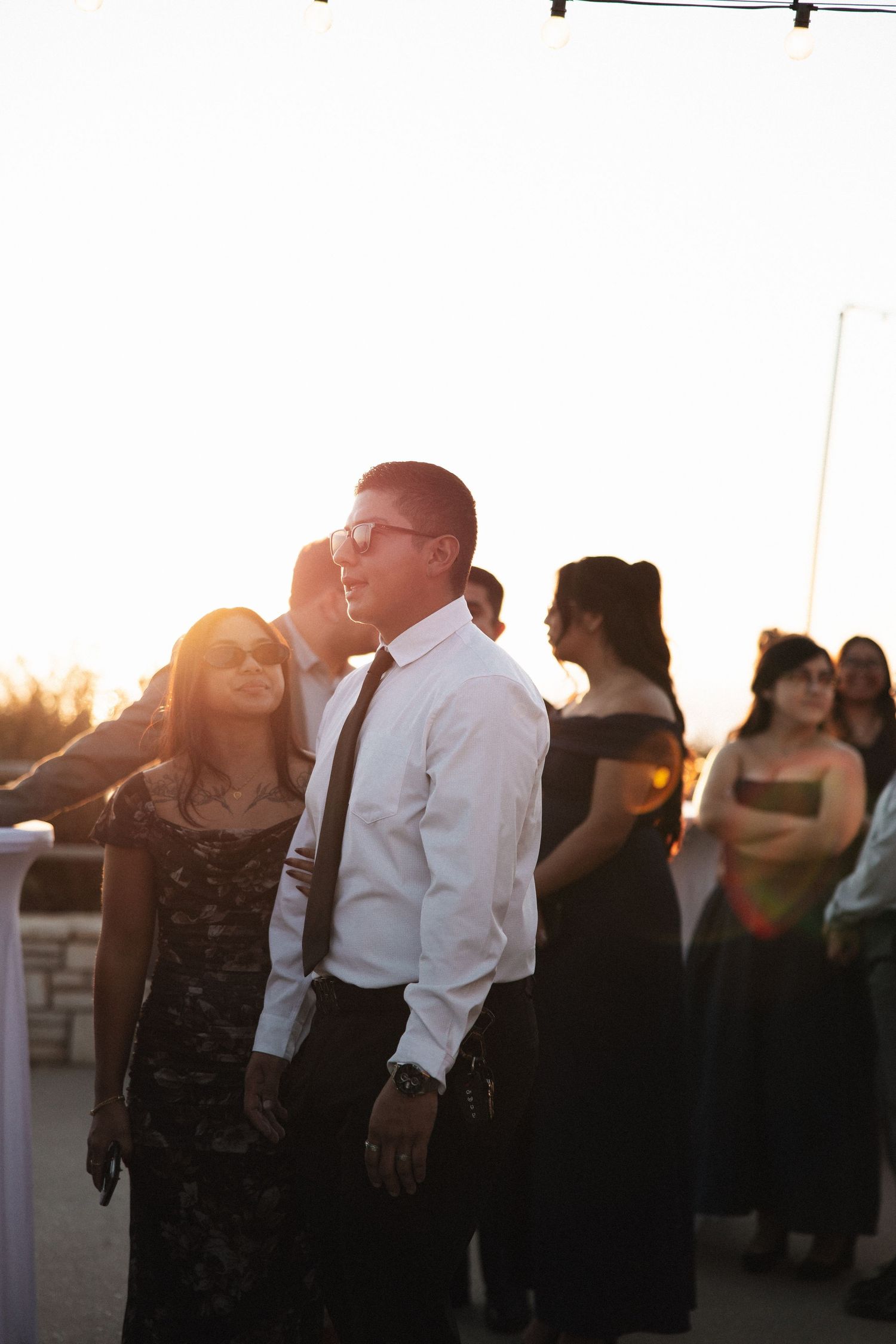 Wedding guests dance together at an outdoor reception during golden hour sunset.