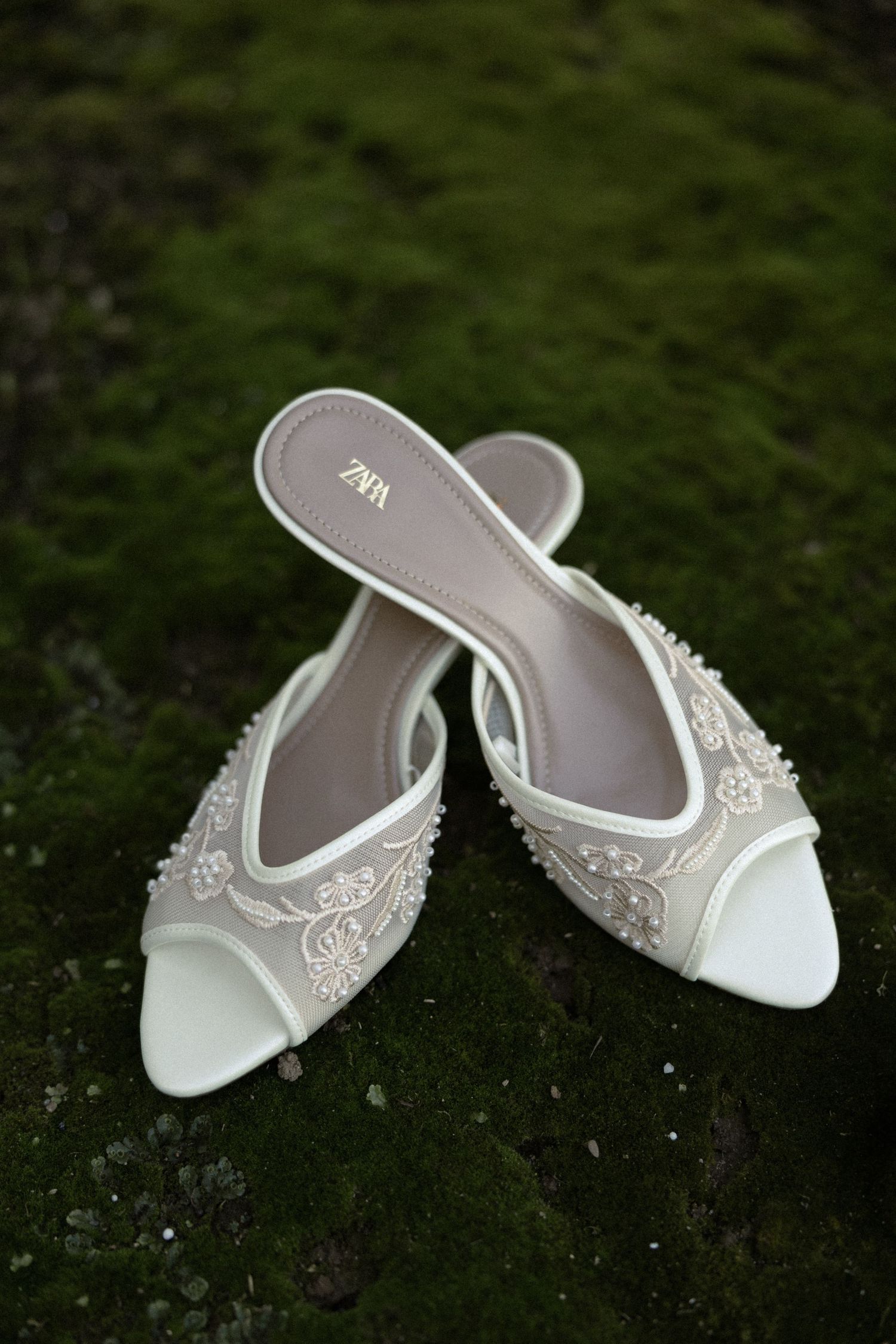 Elegant white bridal slippers with delicate lace embellishments displayed on a dark surface.