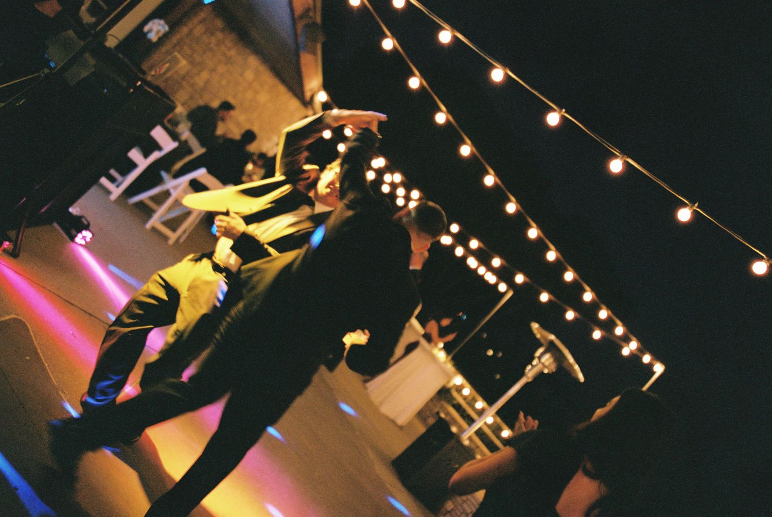 String lights illuminate a dance studio where people practice contemporary dance moves in a dimly lit space.