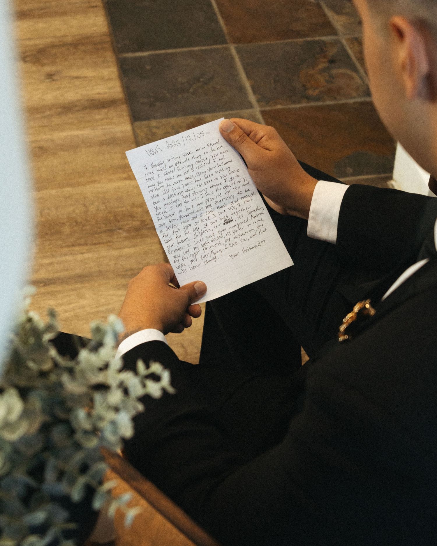 Close-up view of hands holding handwritten wedding vows on white paper during a ceremony.