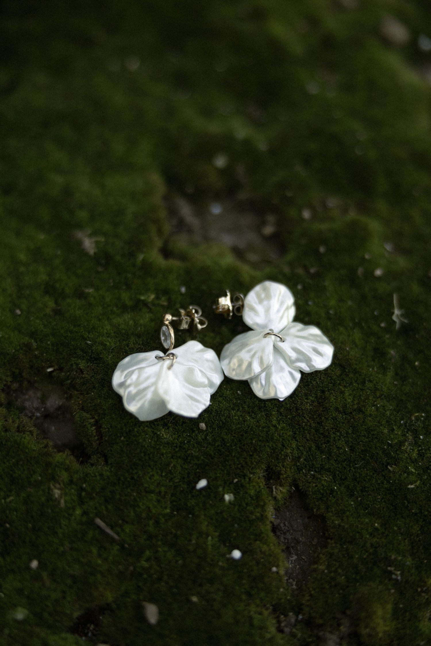 Delicate white fabric flower earrings displayed on green mossy surface with natural lighting.