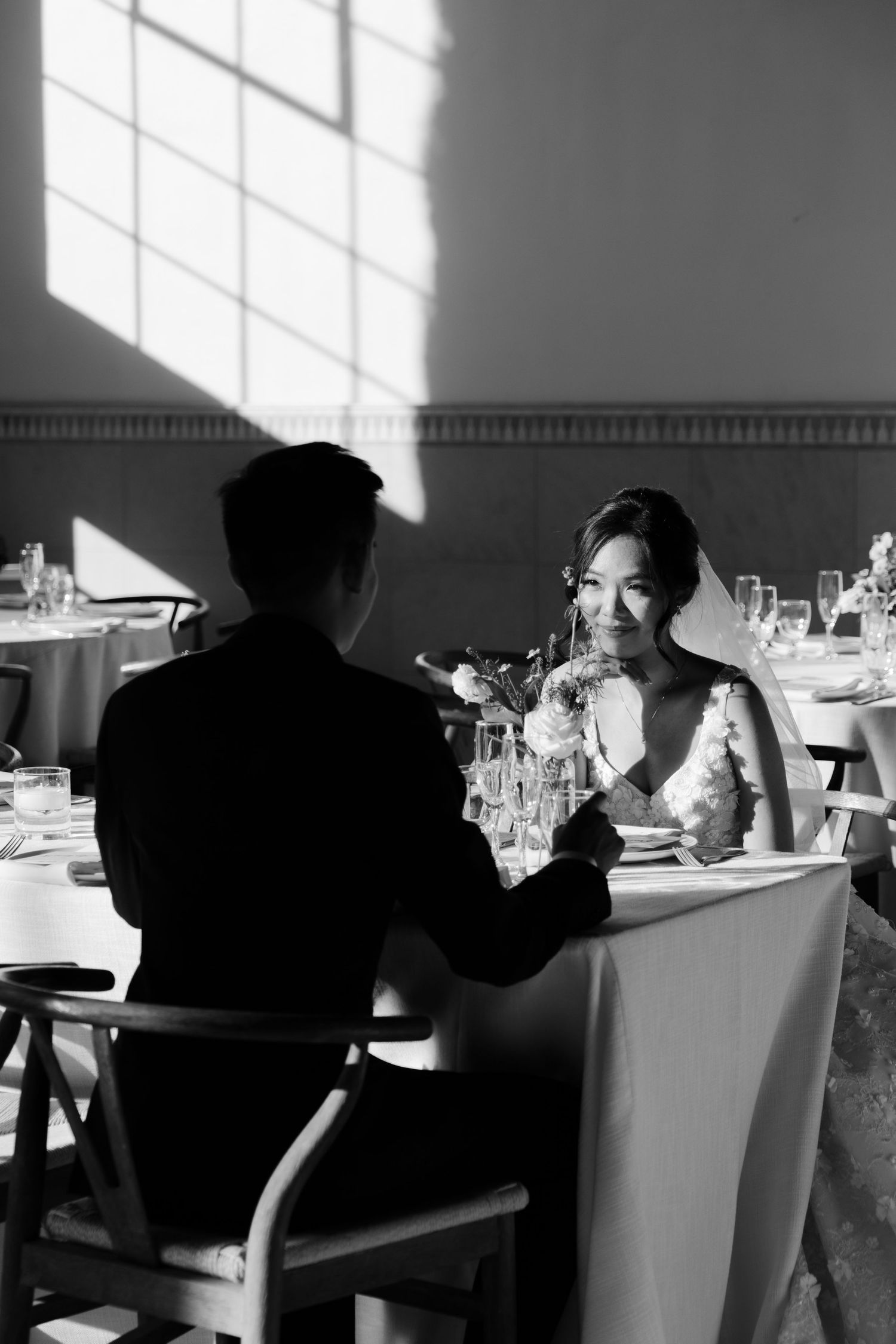 A romantic black and white dinner scene with light streaming through window panes onto an intimate table setting.