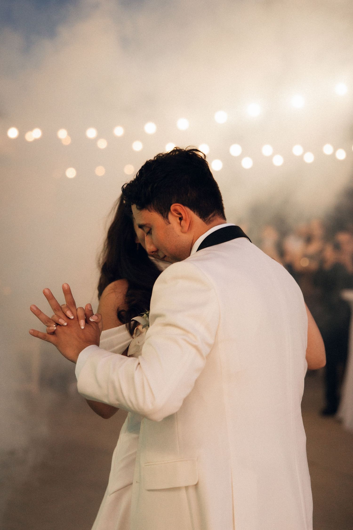 A couple shares their first dance at a wedding reception with romantic string lights and fog in the background.